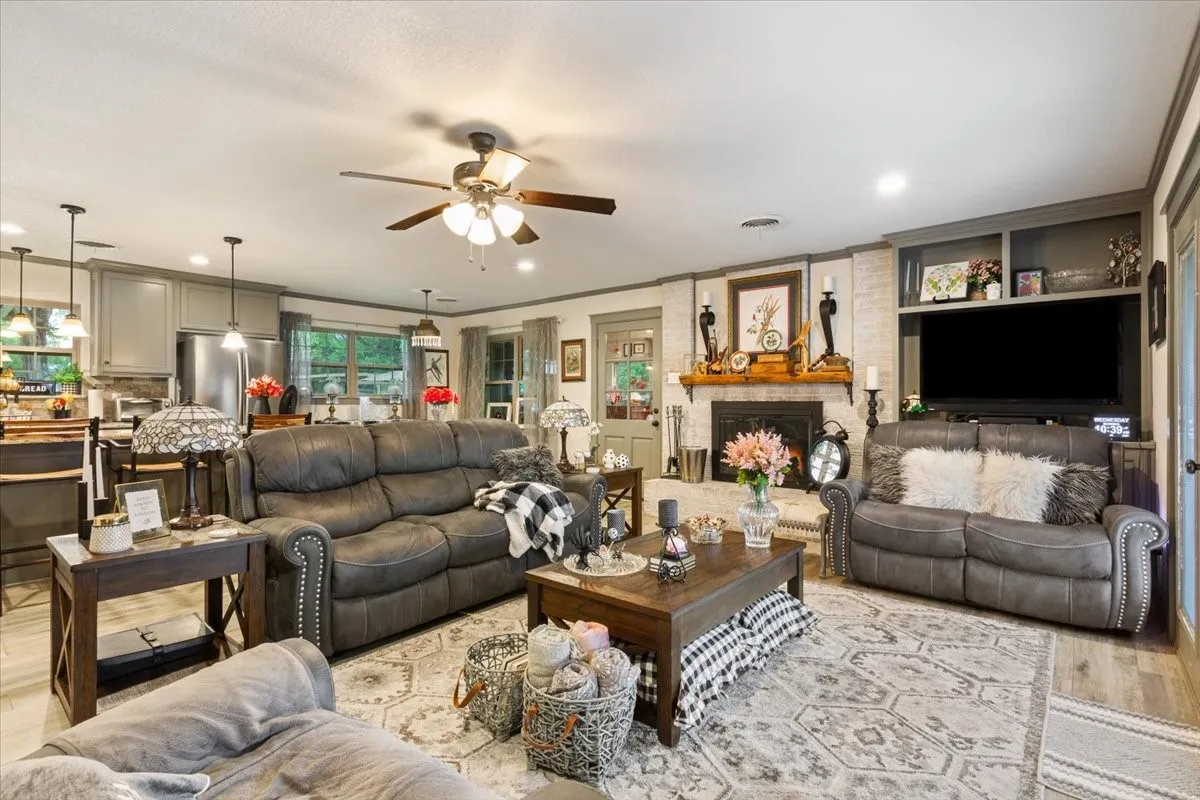 Living room featuring wood finished floors, a fireplace, ornamental molding, ceiling fan, and recessed lighting