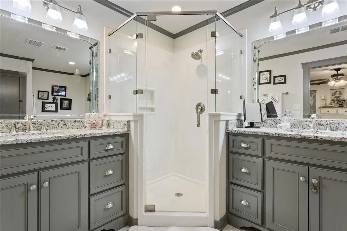 Bathroom with ornamental molding, a shower stall, two vanities, and ceiling fan
