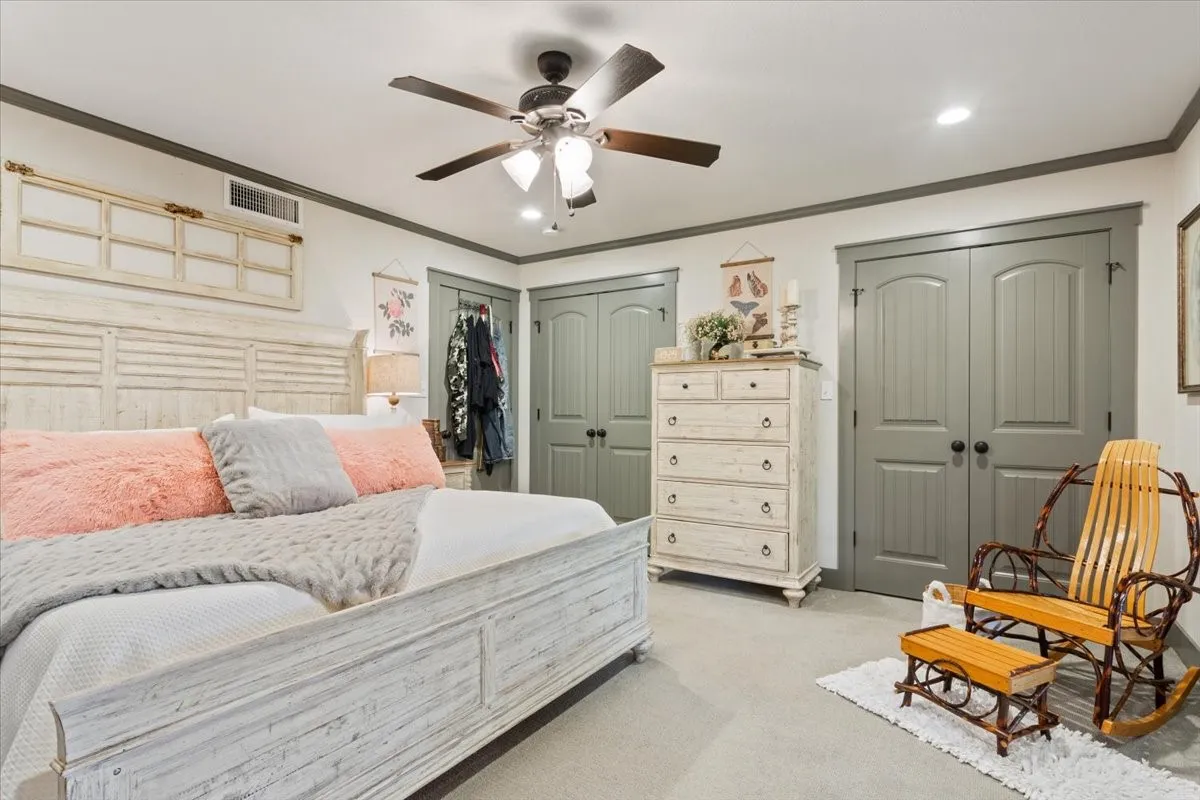 Bedroom featuring ornamental molding, multiple closets, ceiling fan, and light colored carpet
