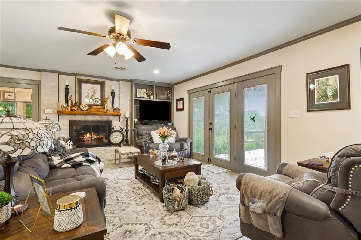 Living room with ornamental molding, built in shelves, a fireplace, and ceiling fan