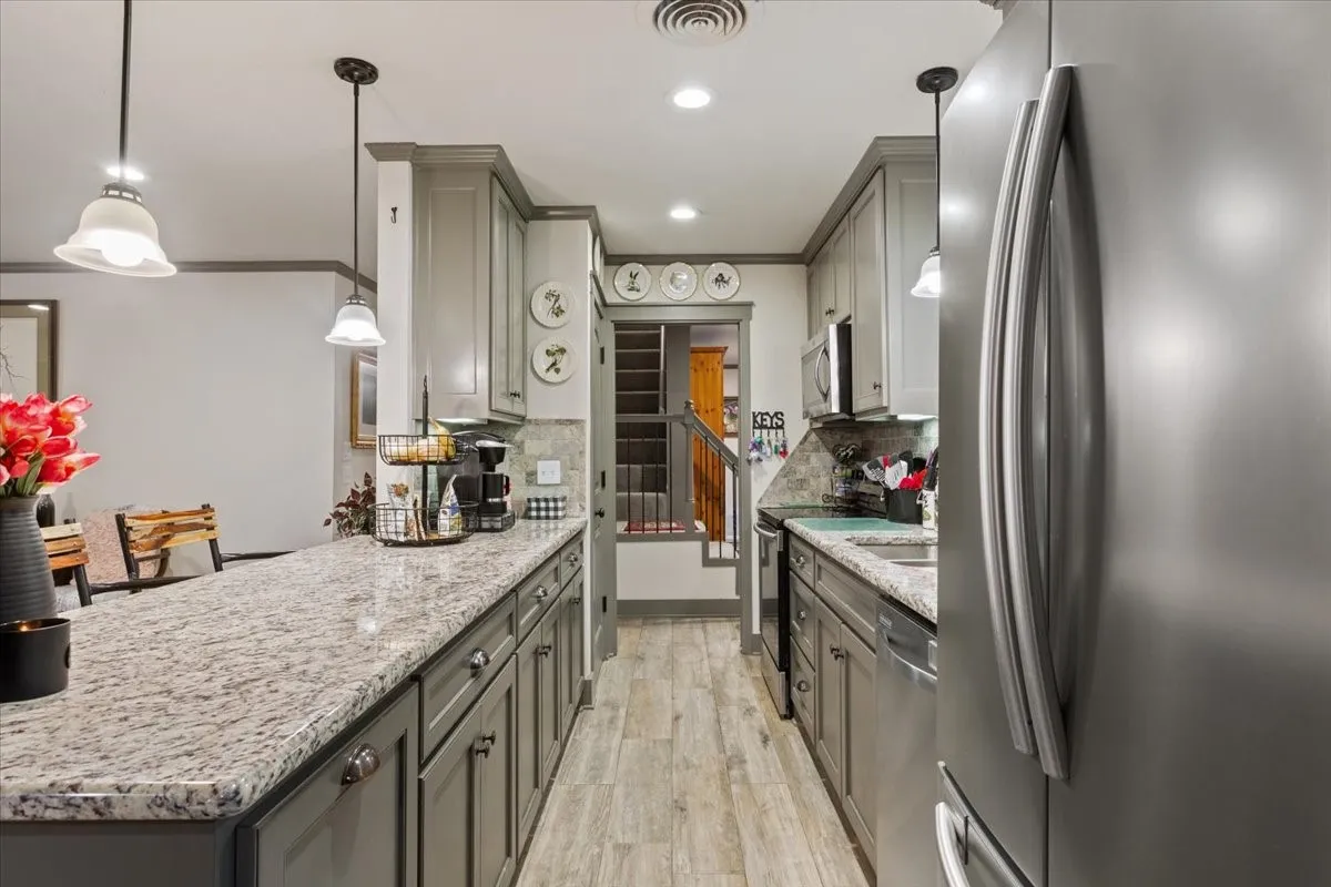Kitchen with stainless steel appliances, light stone countertops, decorative light fixtures, gray cabinets, and light wood finished floors
