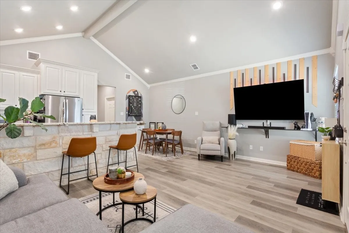 Living room featuring light wood finished floors, beamed ceiling, recessed lighting, ornamental molding, and high vaulted ceiling