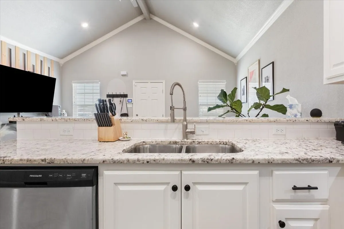 Kitchen with dishwasher, light stone counters, white cabinetry, open floor plan, and ornamental molding