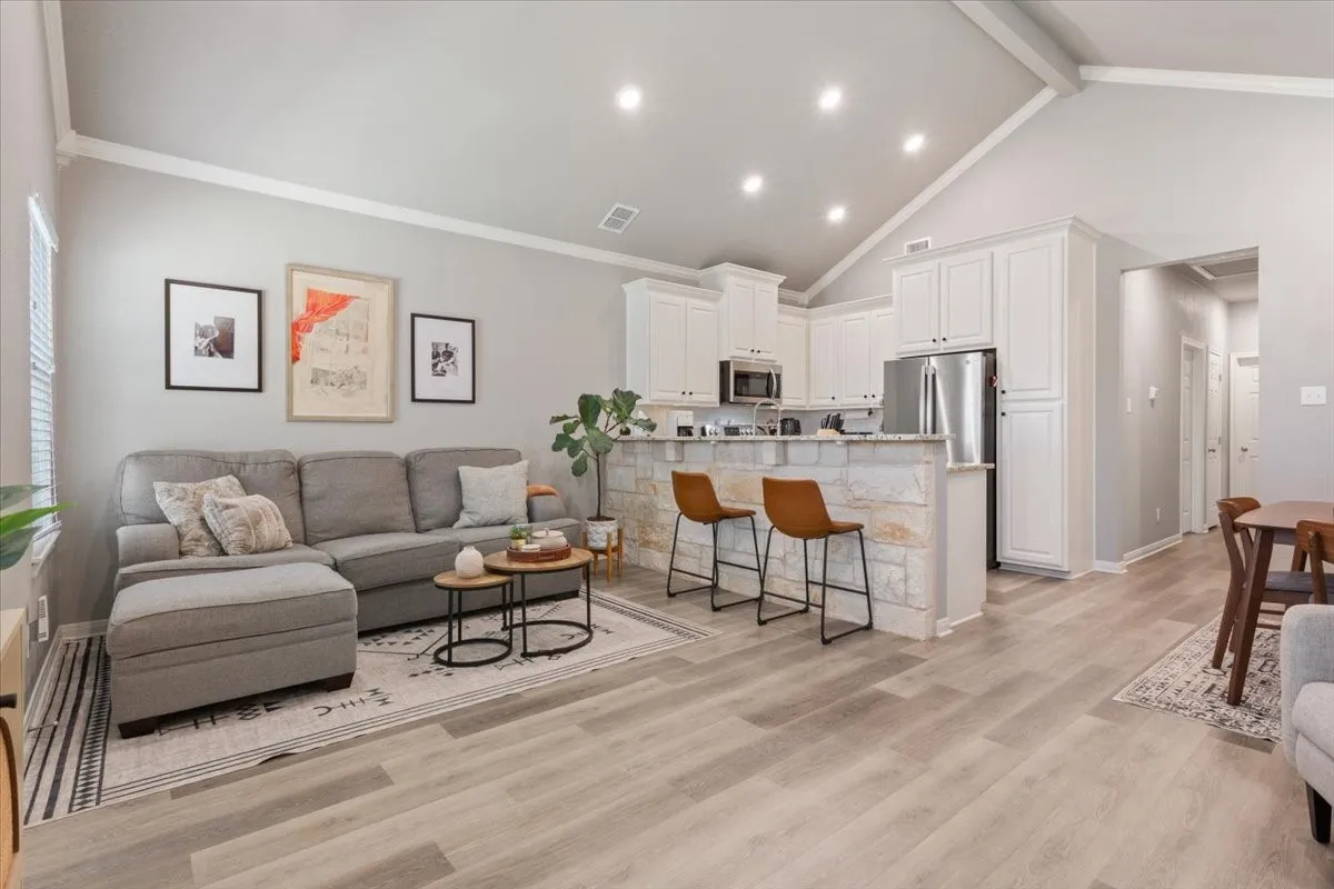 Living area featuring ornamental molding, high vaulted ceiling, light wood-type flooring, and beam ceiling