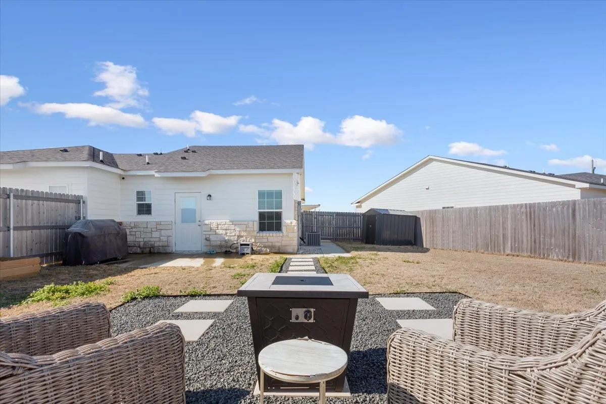 Rear view of property with a patio area, stone siding, a fenced backyard, an outdoor fire pit, and a shingled roof