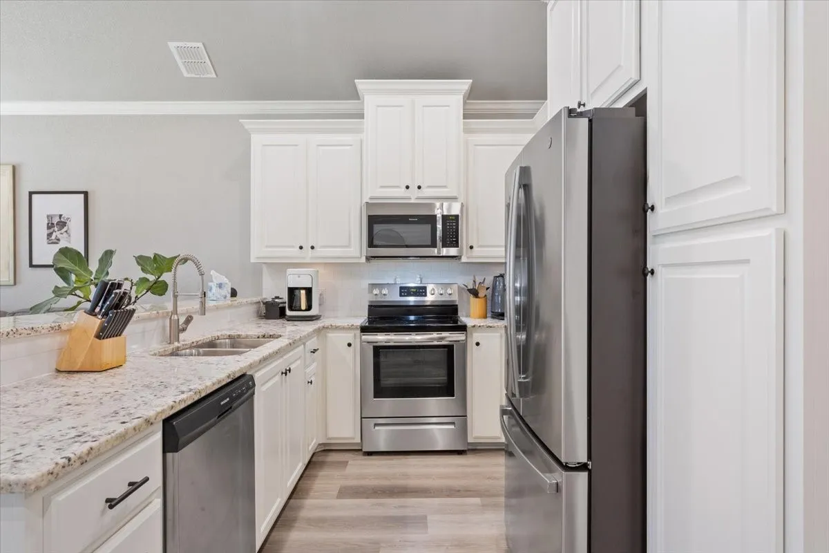 Kitchen featuring stainless steel appliances, light stone counters, white cabinets, crown molding, and light wood finished floors