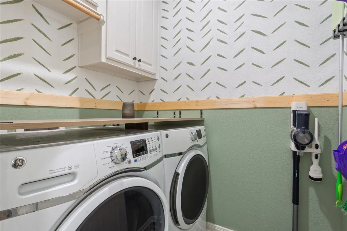 Laundry area featuring washing machine and clothes dryer, cabinet space, and a textured wall
