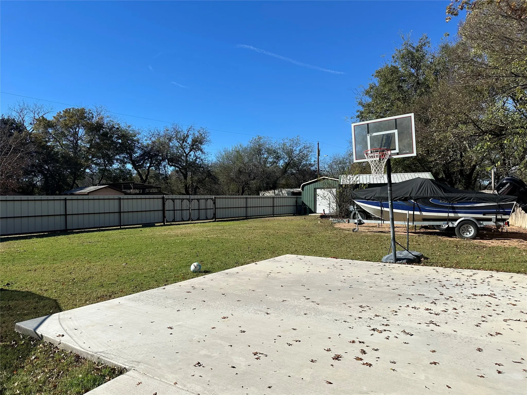 Fenced backyard featuring a storage shed, basketball hoop, and a patio area