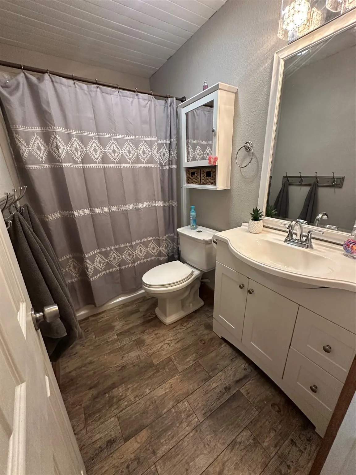 Full bath featuring vanity, a textured wall, curtained shower, and dark wood-style flooring