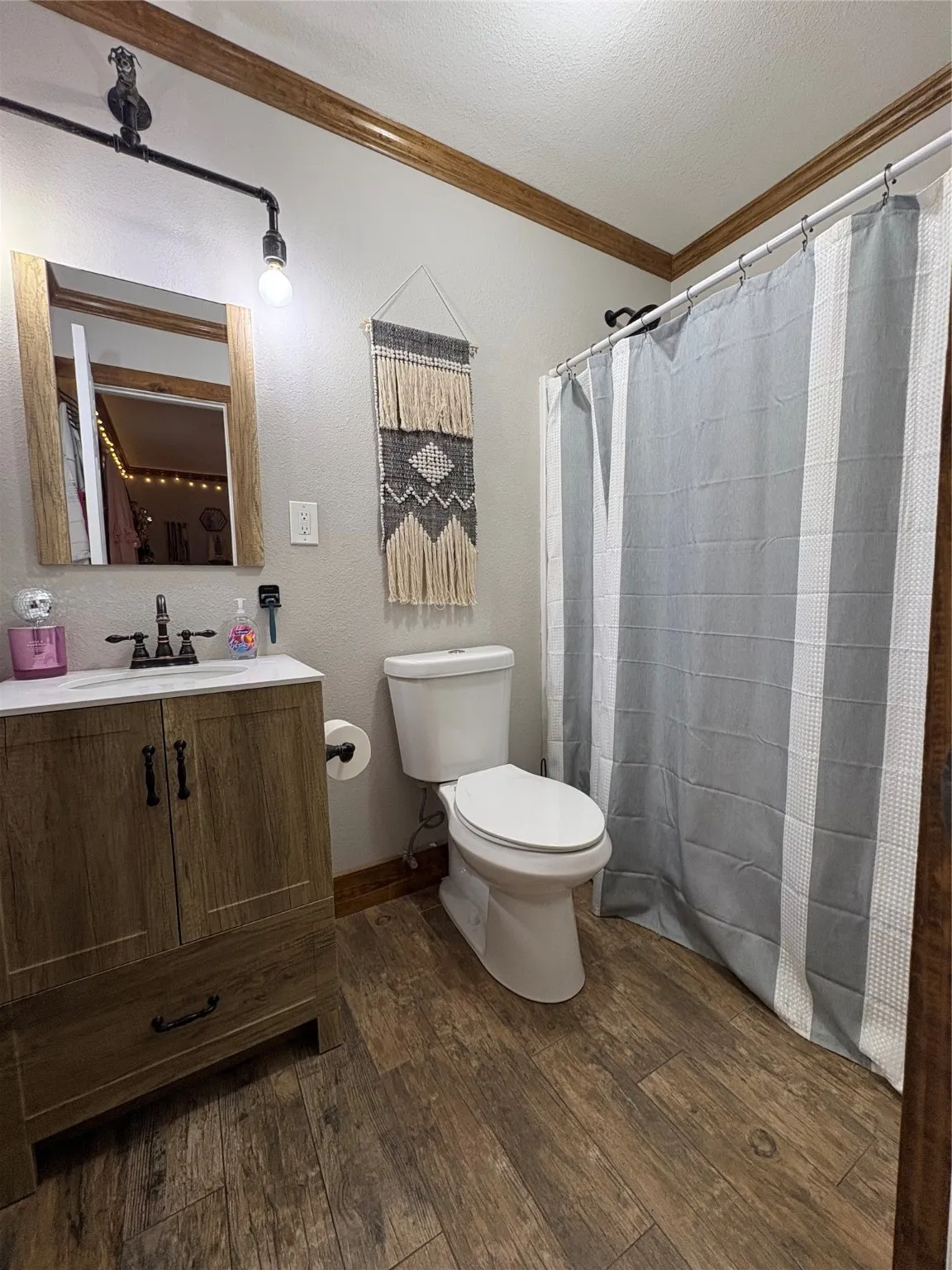 Bathroom with ornamental molding, dark wood-style flooring, curtained shower, vanity, and a textured wall