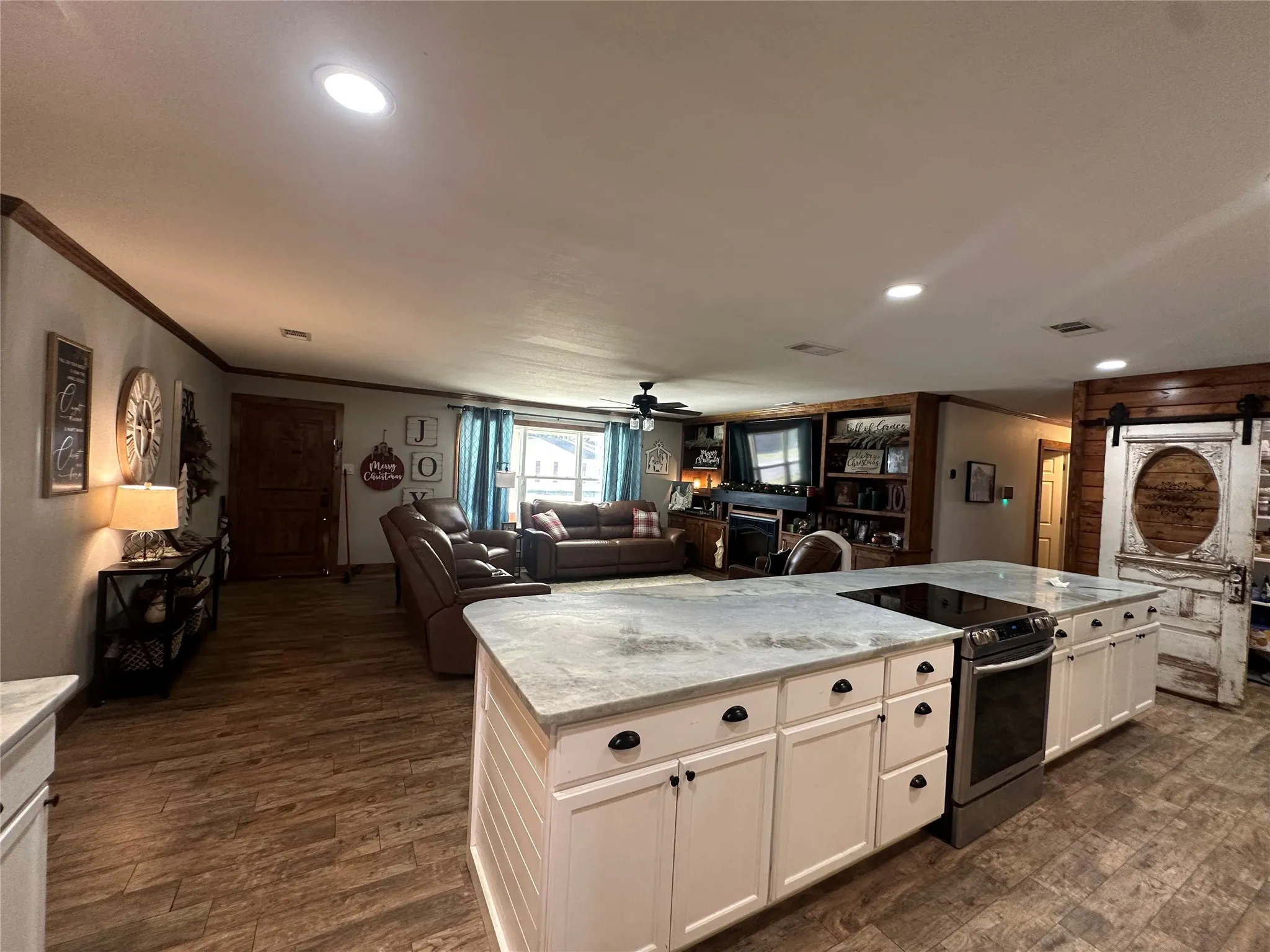 Kitchen featuring stainless steel electric range, a barn door, light stone counters, a ceiling fan, and a fireplace