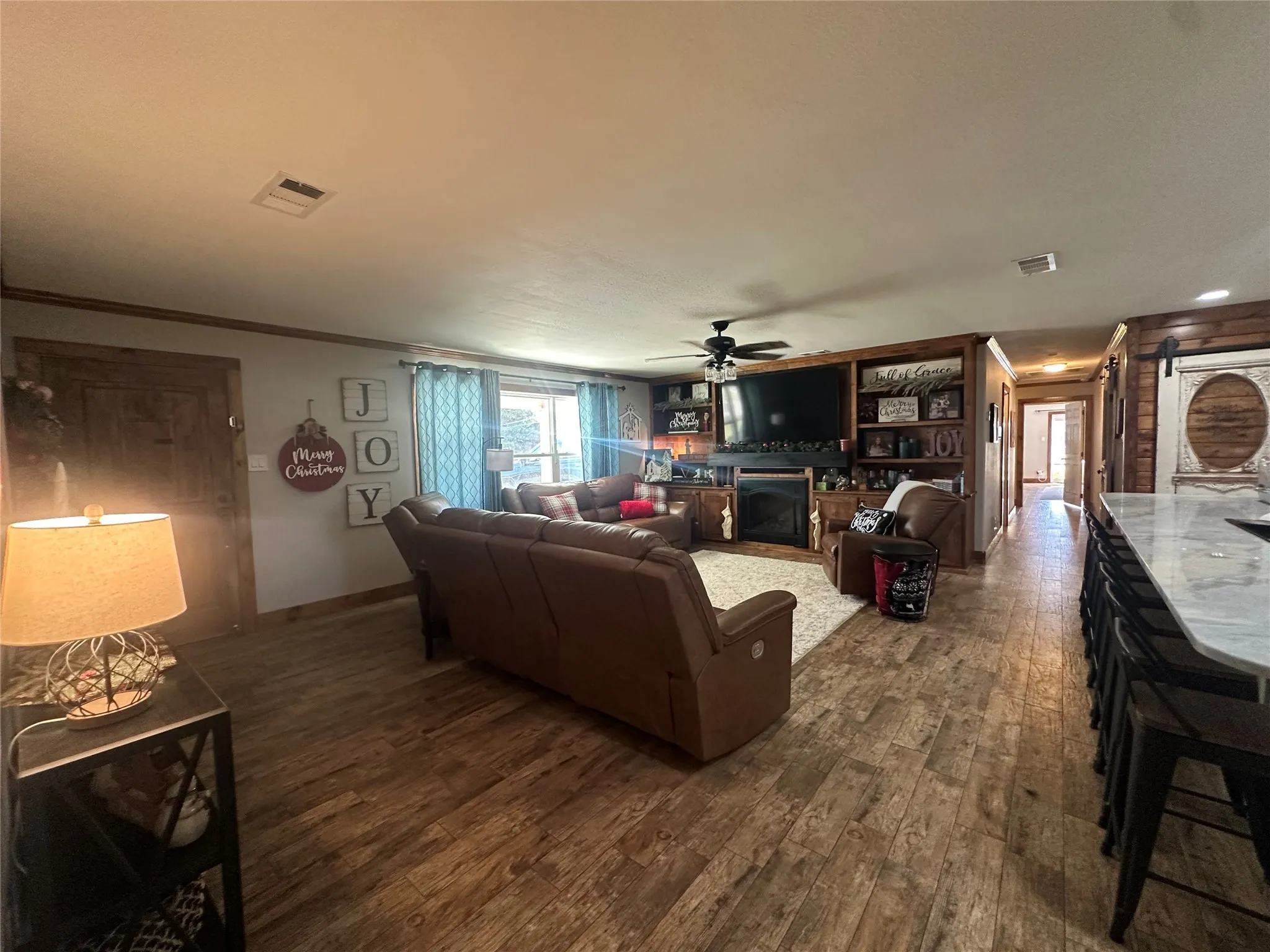 Living room with a barn door, hardwood / wood-style floors, ceiling fan, a fireplace, and ornamental molding