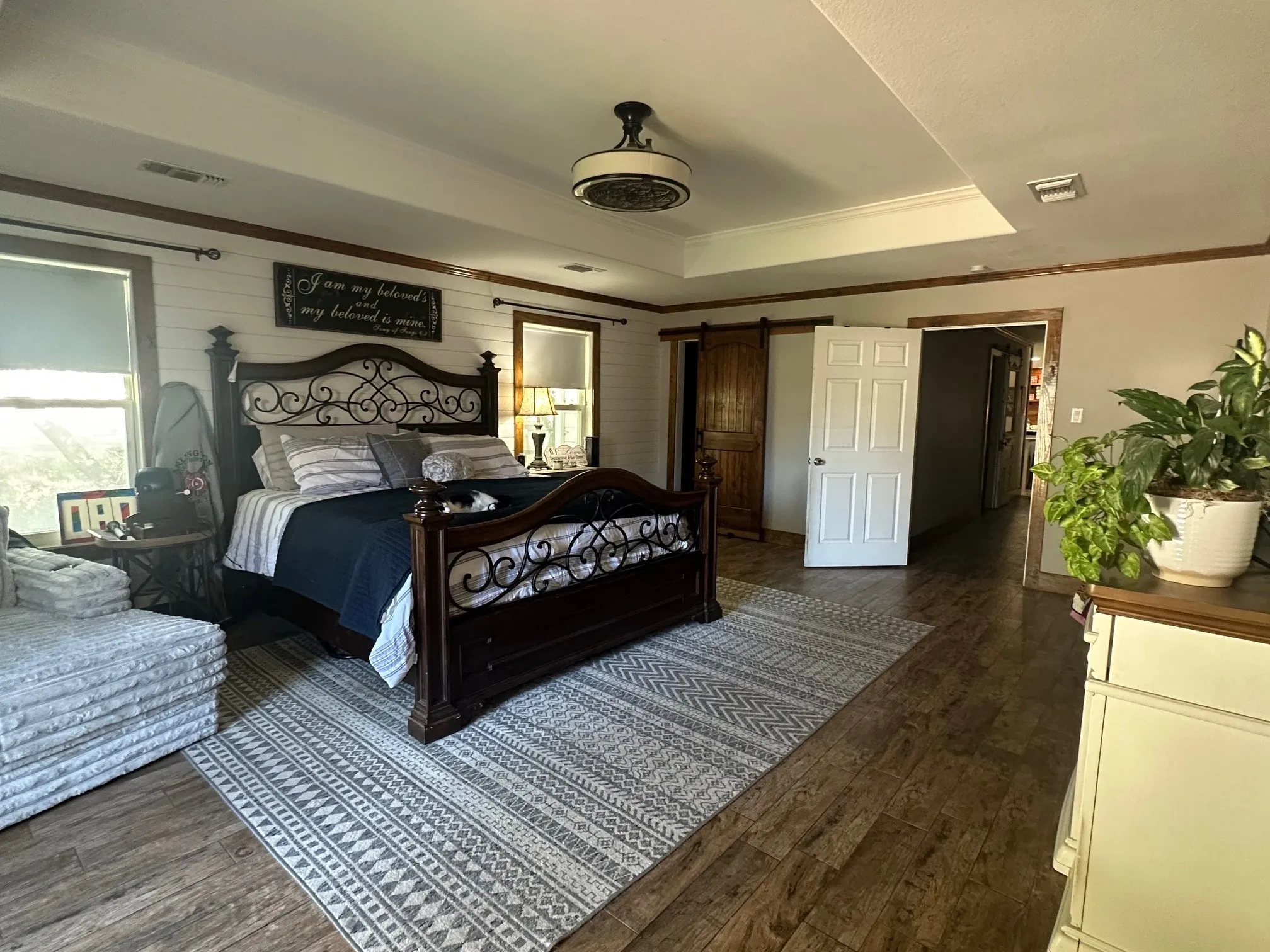 Bedroom with a barn door, a tray ceiling, dark wood-style floors, crown molding, and wooden walls