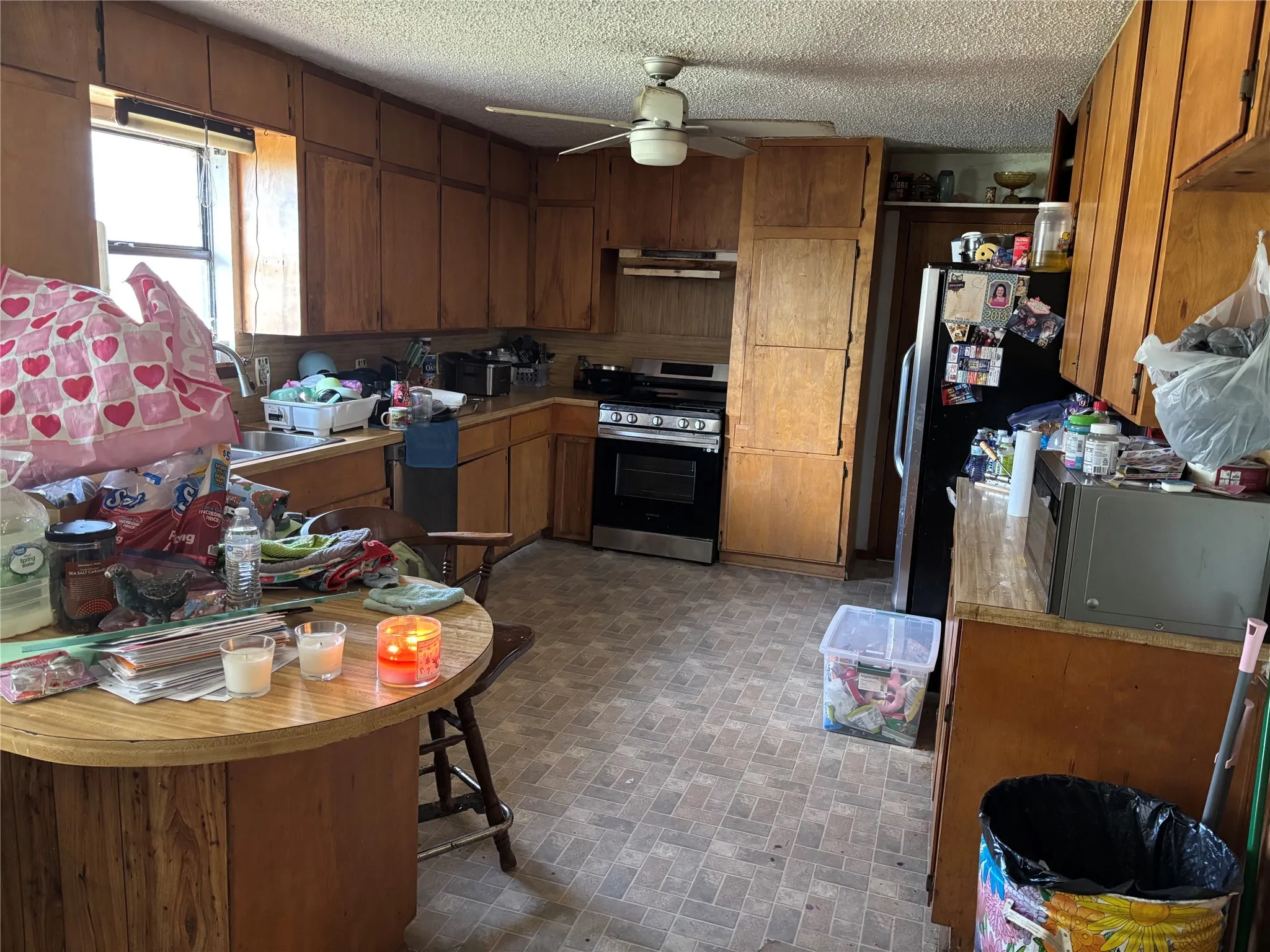 Kitchen with brick patterned floors, appliances with stainless steel finishes, open shelves, brown cabinets, and light countertops