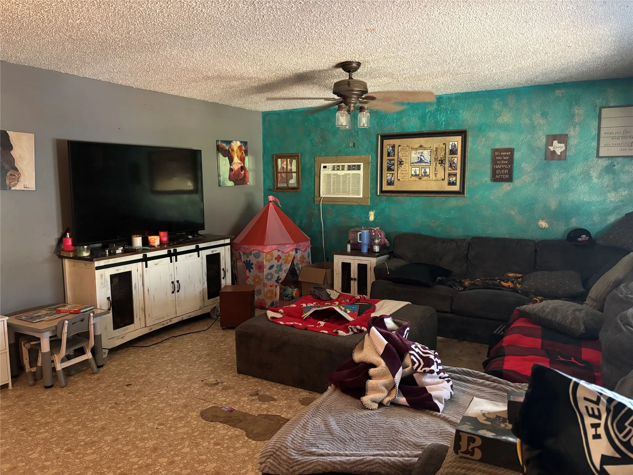 Living room with a textured ceiling, ceiling fan, and a wall mounted air conditioner
