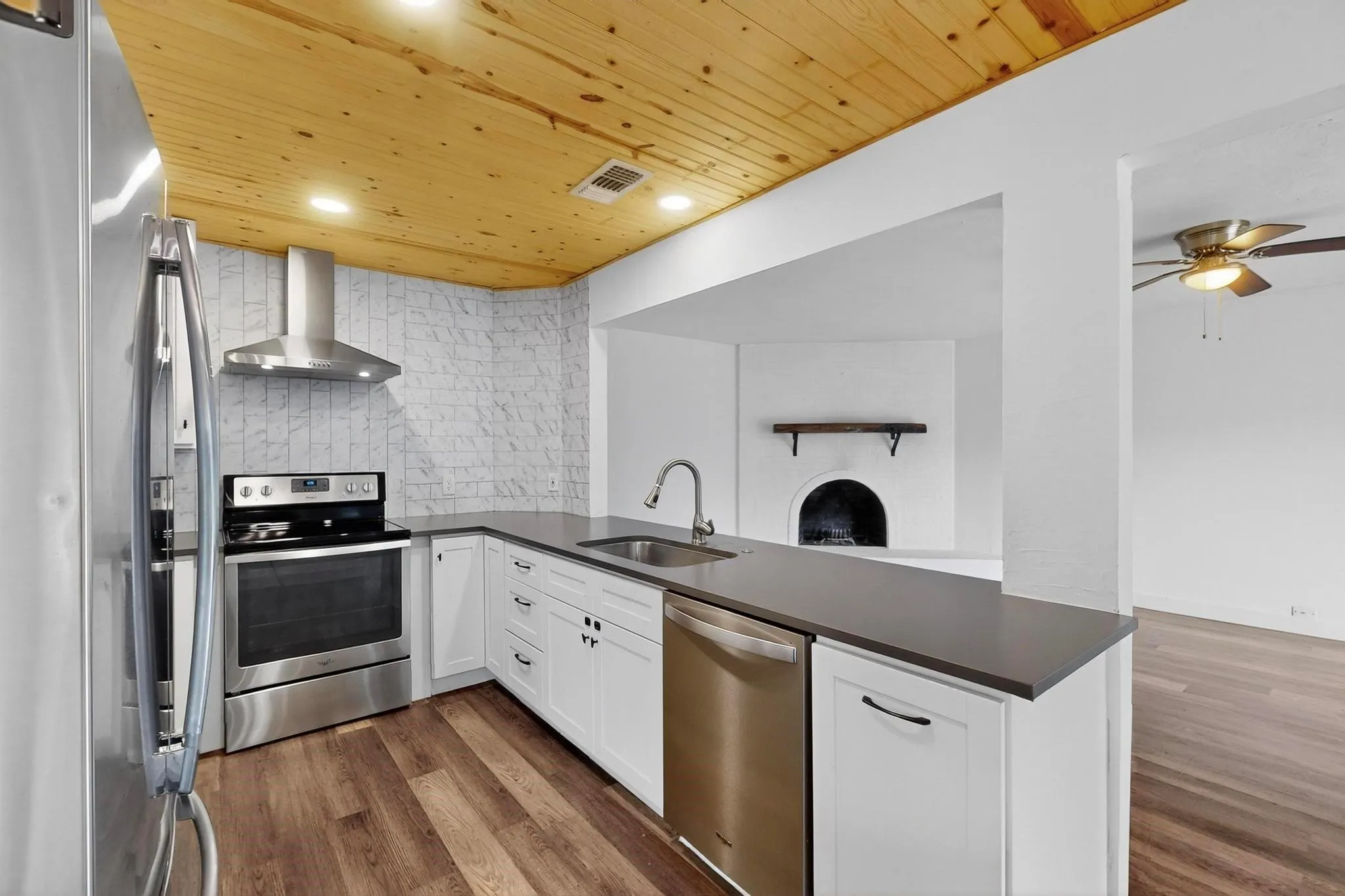 Kitchen featuring a peninsula, stainless steel appliances, wood ceiling, wall chimney exhaust hood, and decorative backsplash