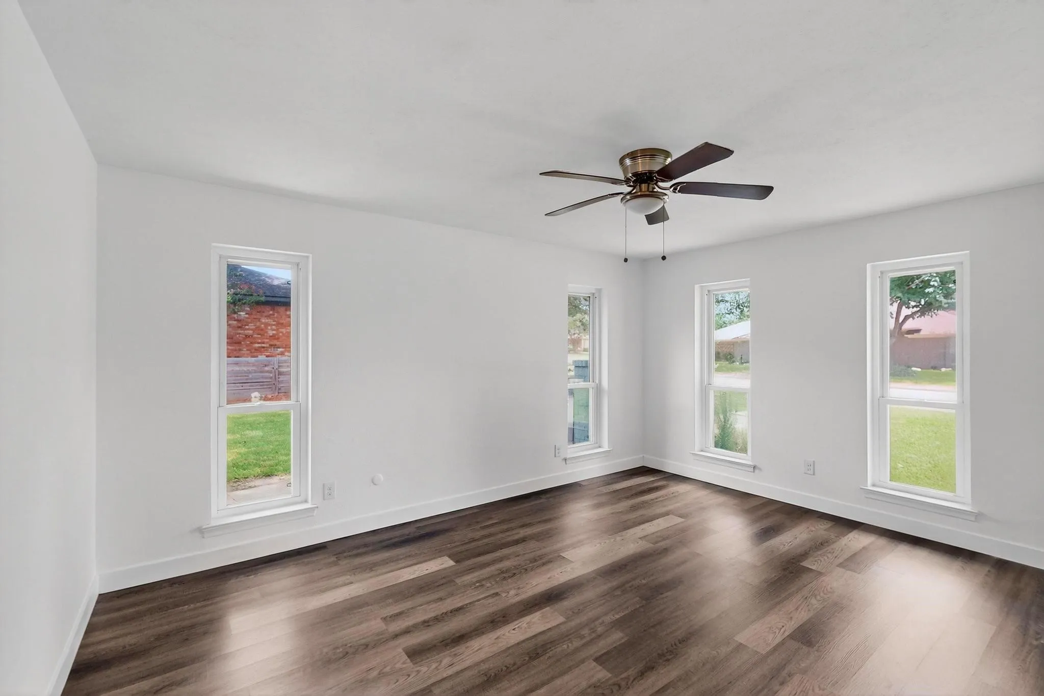 Unfurnished room with dark wood-style floors, healthy amount of natural light, and a ceiling fan