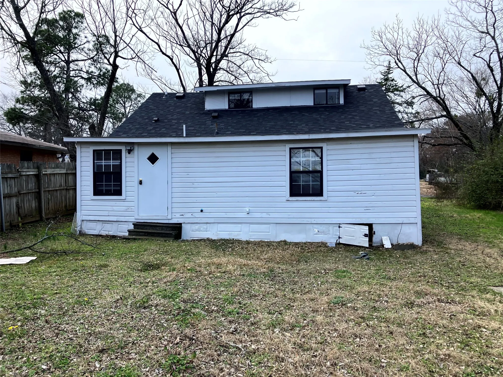 Rear view of property with a shingled roof, entry steps, and crawl space