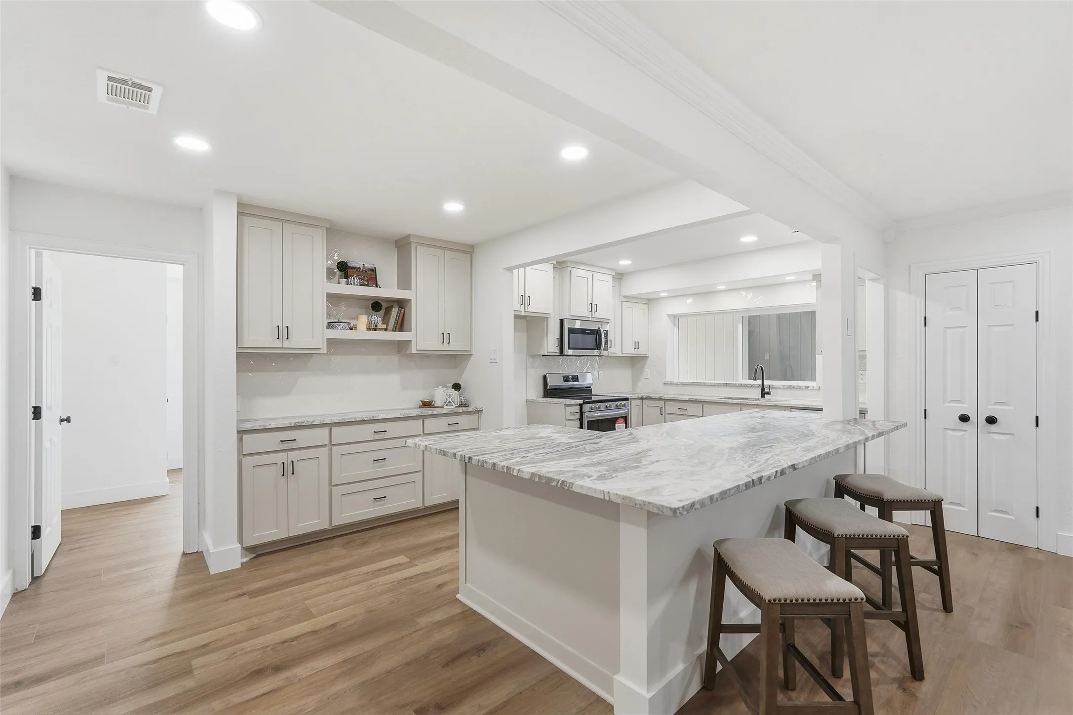 dry bar featuring open shelves, light wood-type flooring, light granite counters, stainless steel appliances, and light painted cabinets