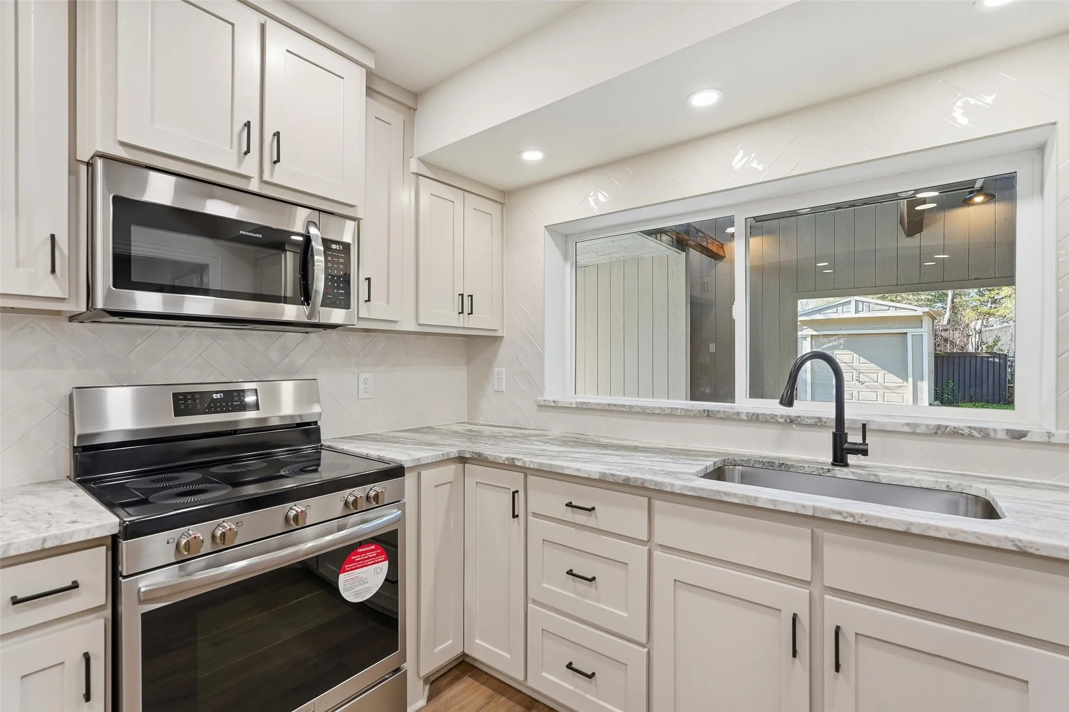 Kitchen with stainless steel appliances, light granite counters, recessed lighting, tasteful backsplash, and light painted cabinetry