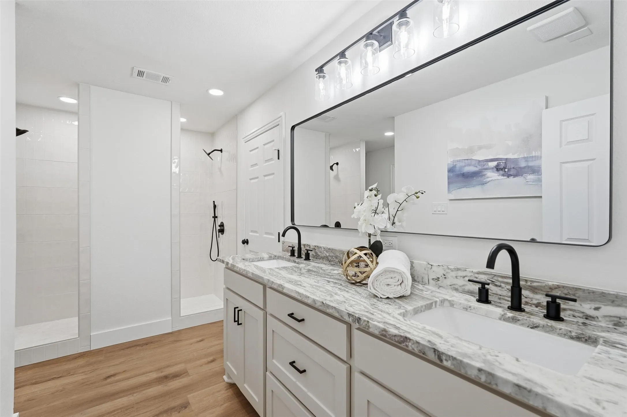 Primary bathroom featuring double vanity, double walk in shower, light wood finished floors, and recessed lighting