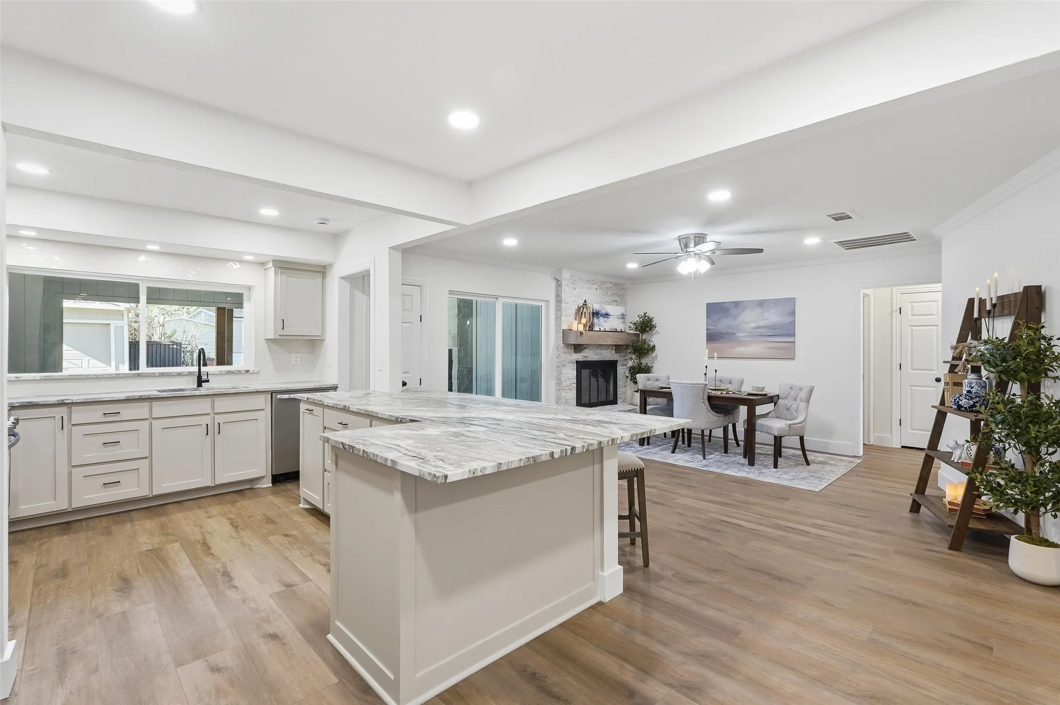 Kitchen with white cabinets, light stone counters, light wood-style flooring, a fireplace, and a ceiling fan