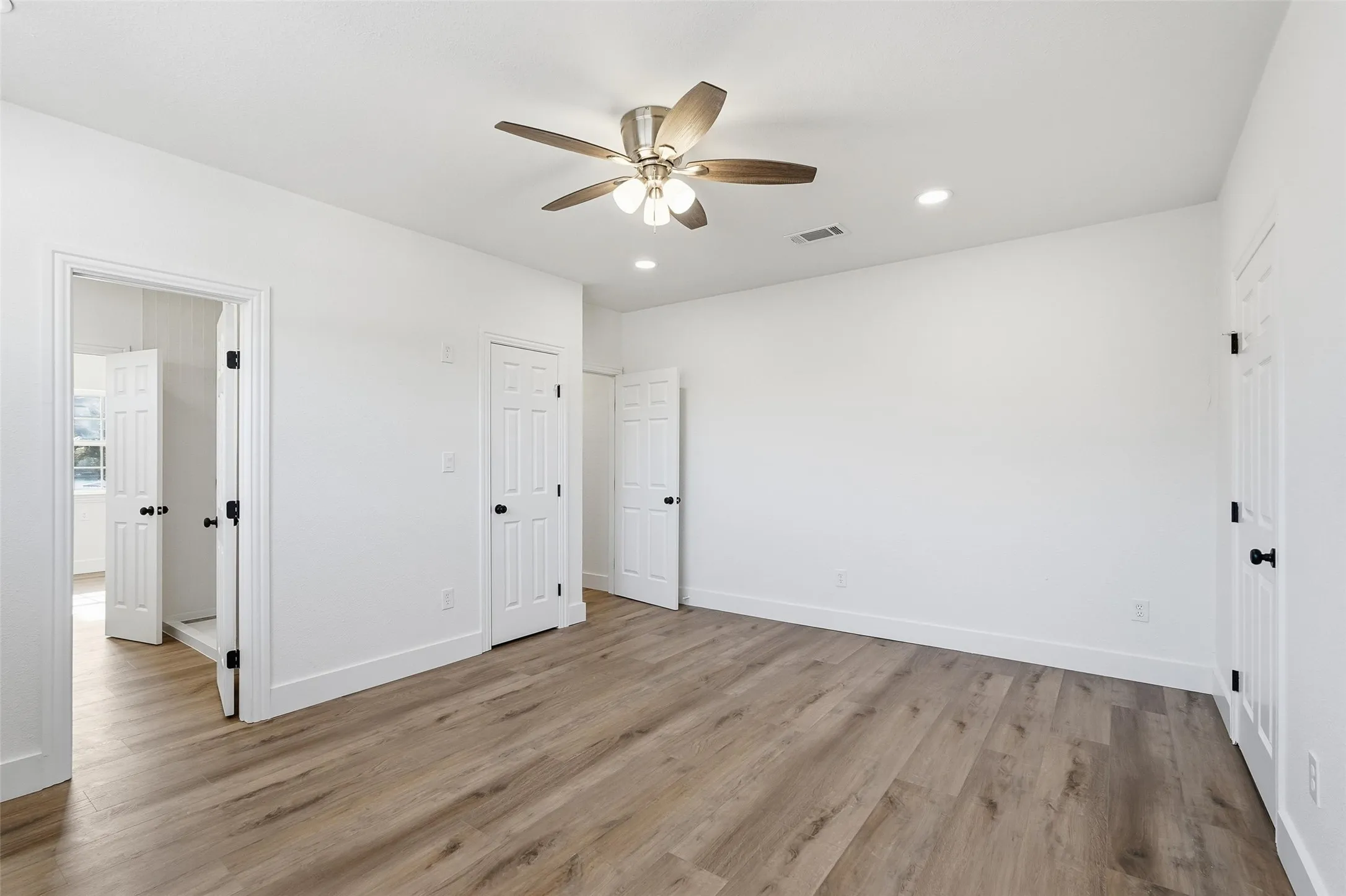 Upstairs bedroom with light wood-style floors, ceiling fan, and recessed lighting