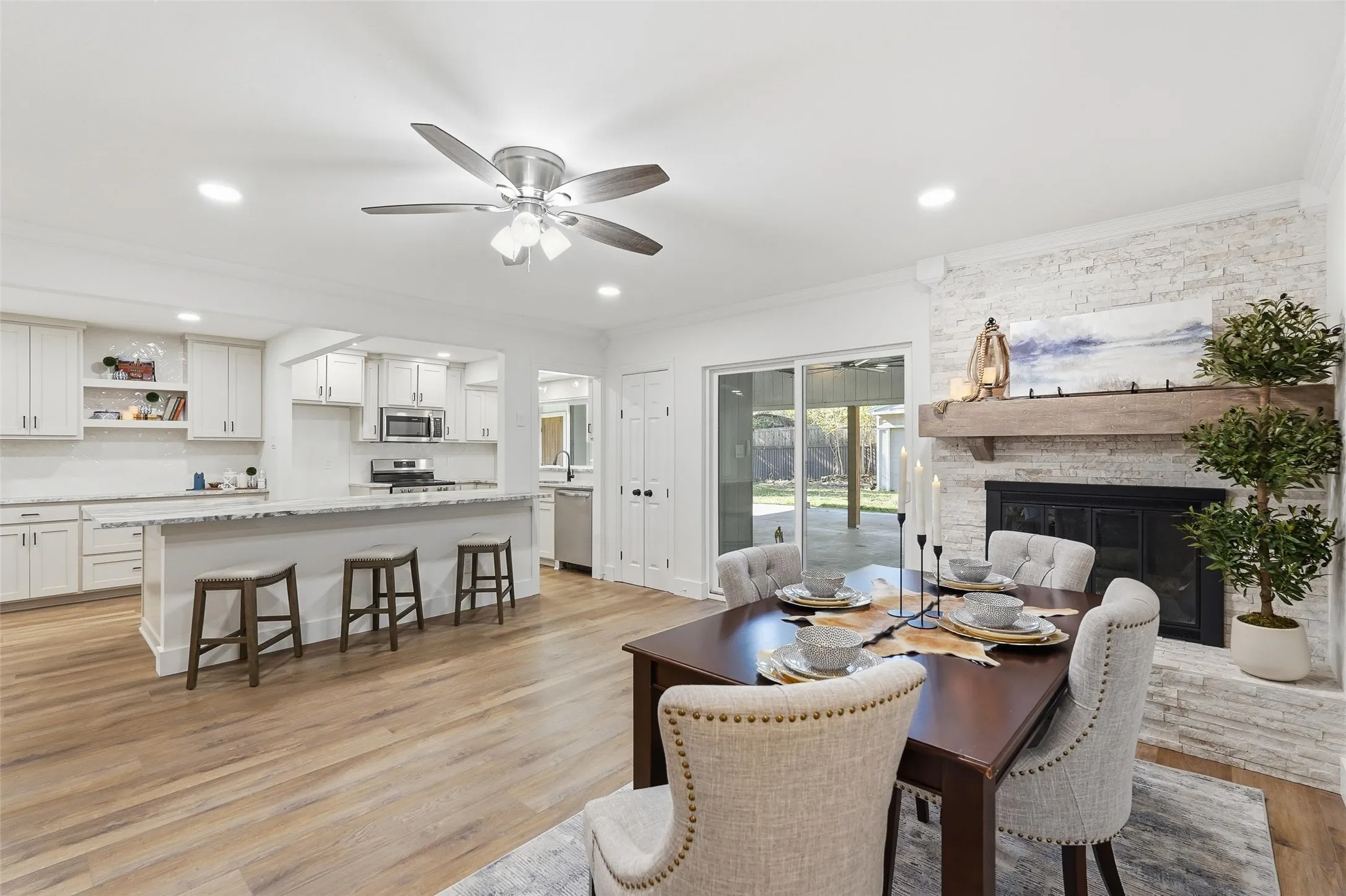 Dining room featuring a fireplace, ceiling fan, light wood-type flooring, recessed lighting, and ornamental molding