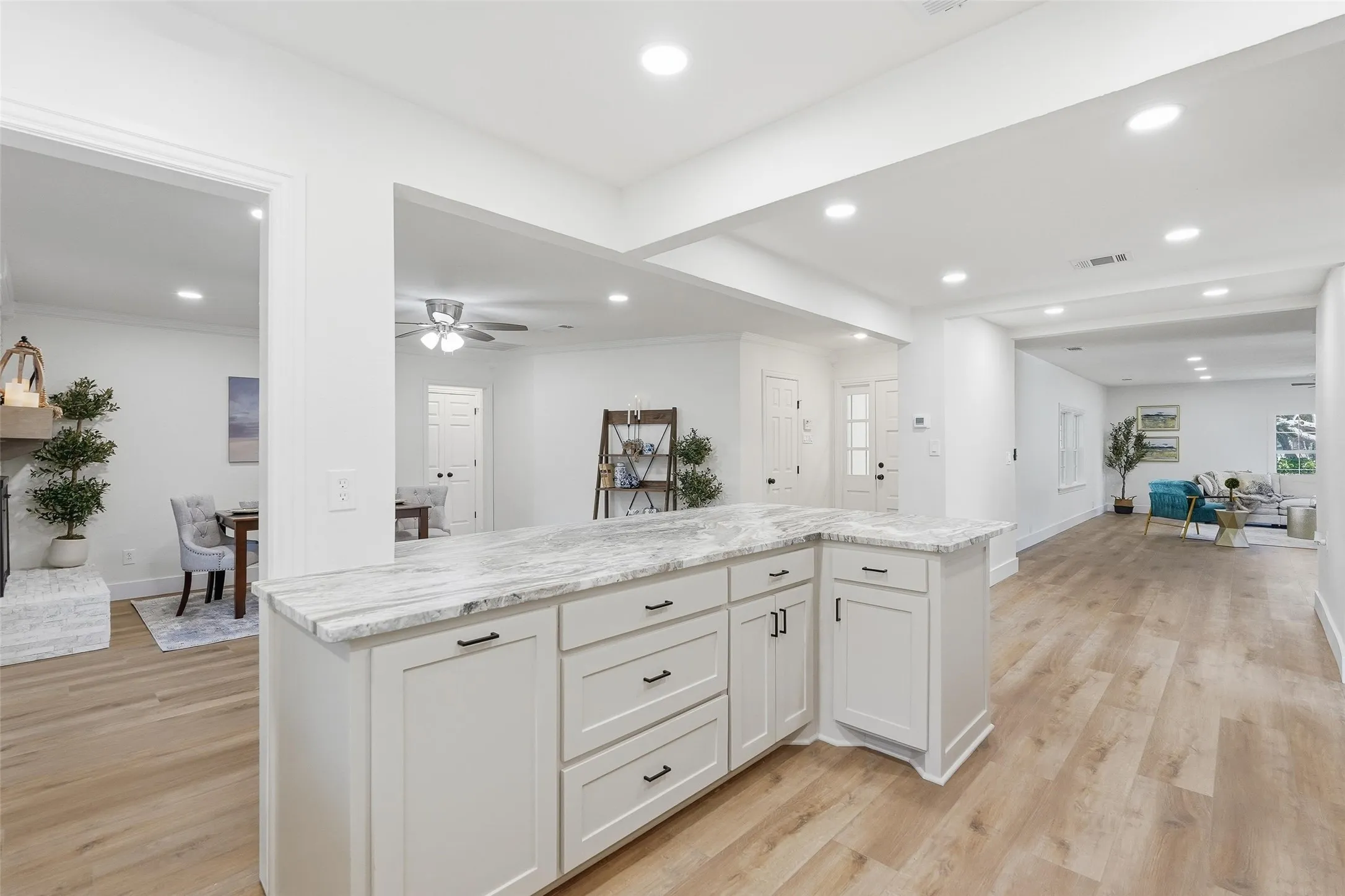 Kitchen featuring open floor plan, white cabinets, light wood-type flooring, a fireplace with raised hearth, and recessed lighting