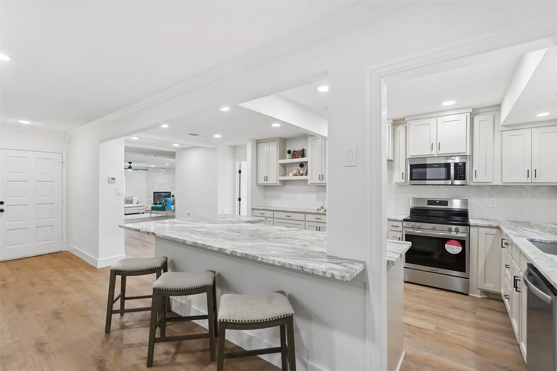 Kitchen featuring light granite countertops, appliances with stainless steel finishes, light painted cabinetry, ornamental molding, and a kitchen breakfast bar