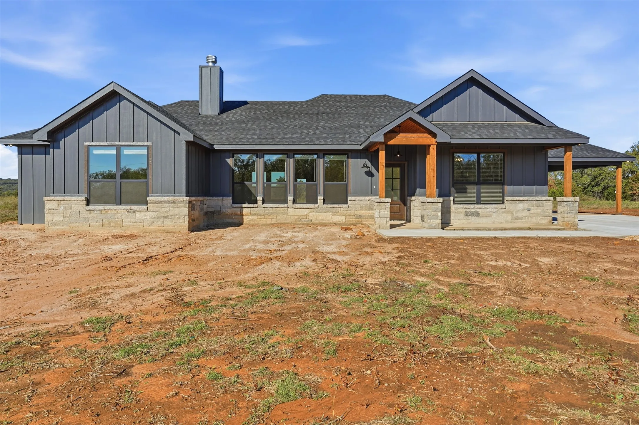 Modern farmhouse with roof with shingles, stone siding, covered porch, a chimney, and board and batten siding