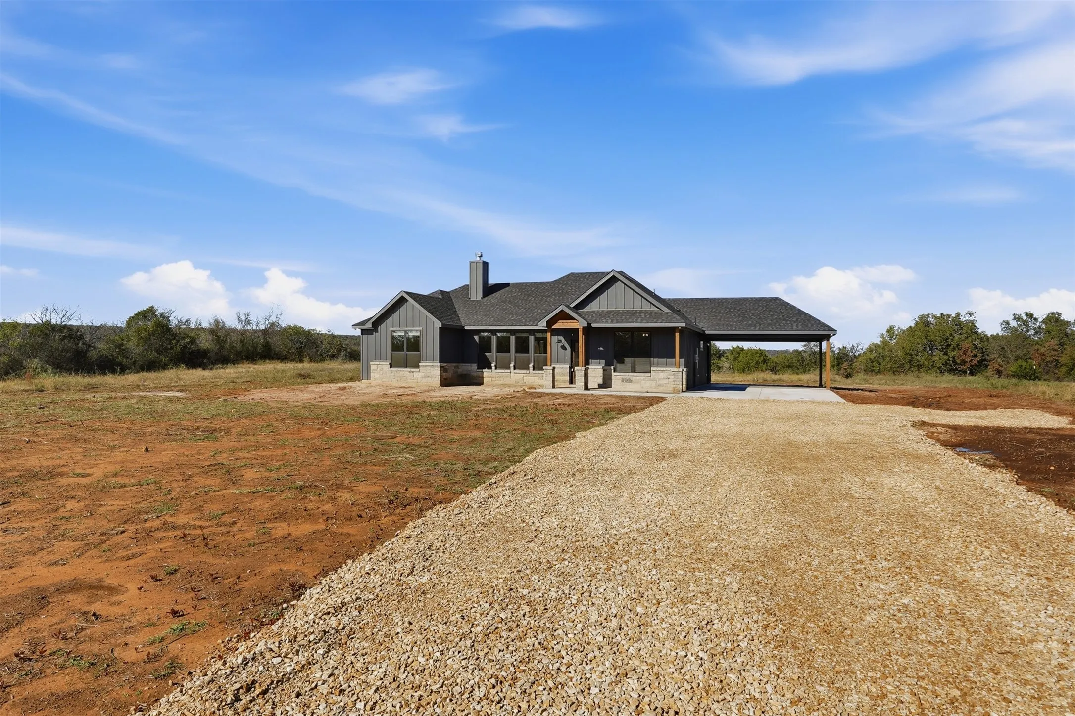 Modern farmhouse style home with a chimney, gravel driveway, a carport, covered porch, and board and batten siding
