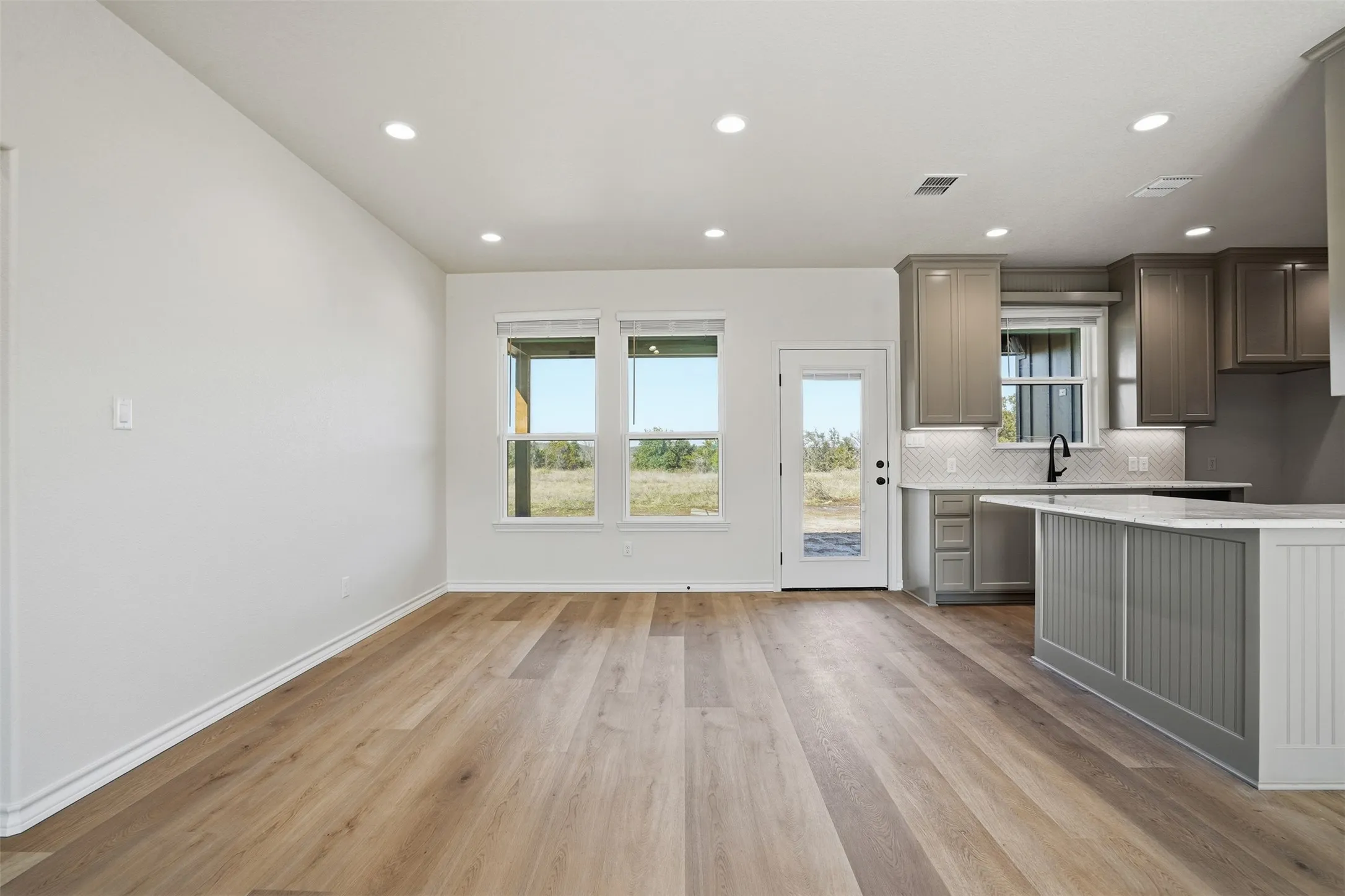 Kitchen featuring light wood-type flooring, tasteful backsplash, gray cabinets, recessed lighting, and light stone countertops