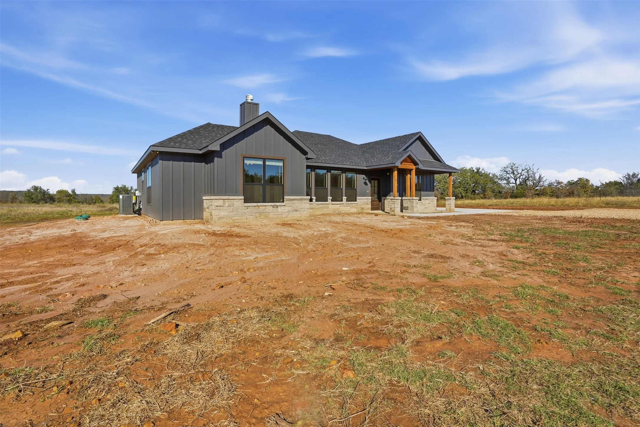 View of front of home with covered porch, a chimney, roof with shingles, and stone siding