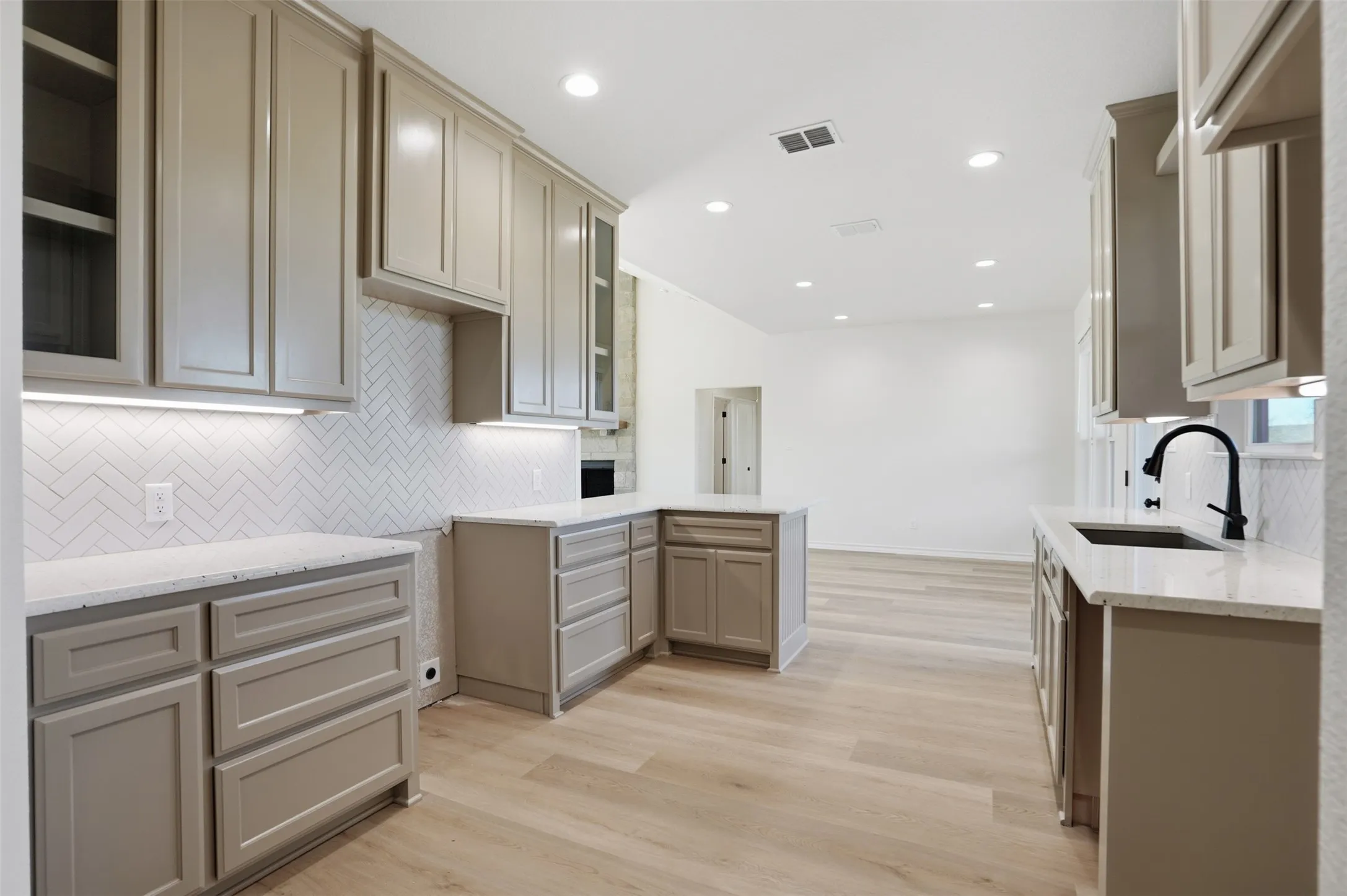 Kitchen featuring a peninsula, tasteful backsplash, light wood-type flooring, light stone countertops, and glass insert cabinets