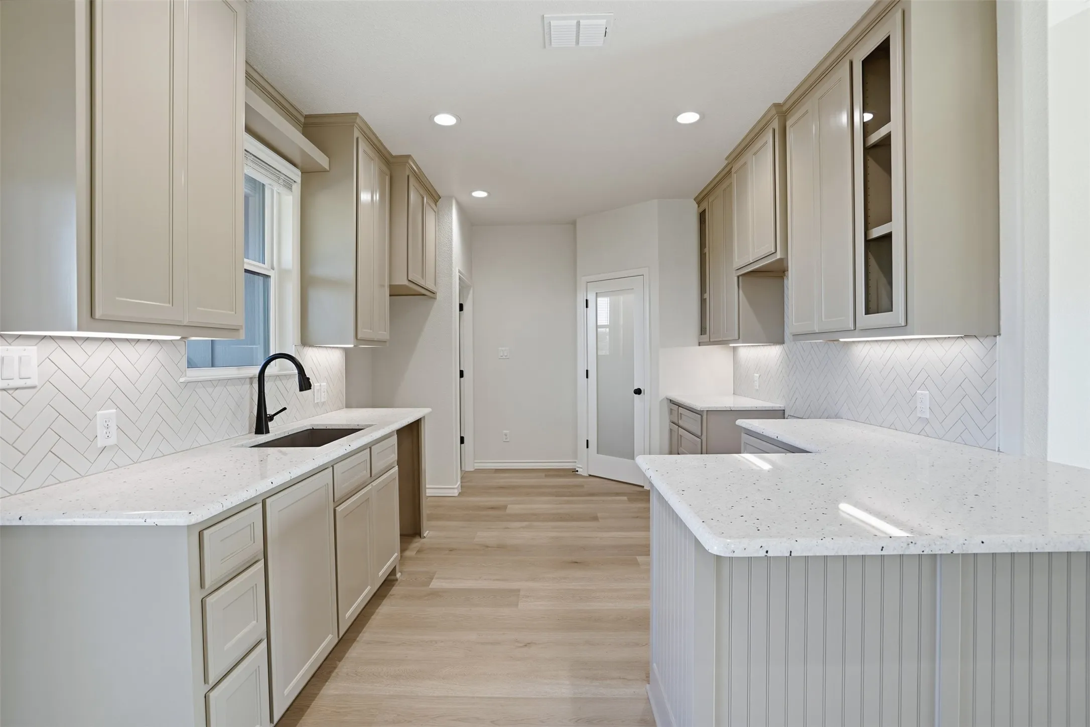 Kitchen featuring backsplash, light stone counters, light wood-style floors, a peninsula, and recessed lighting