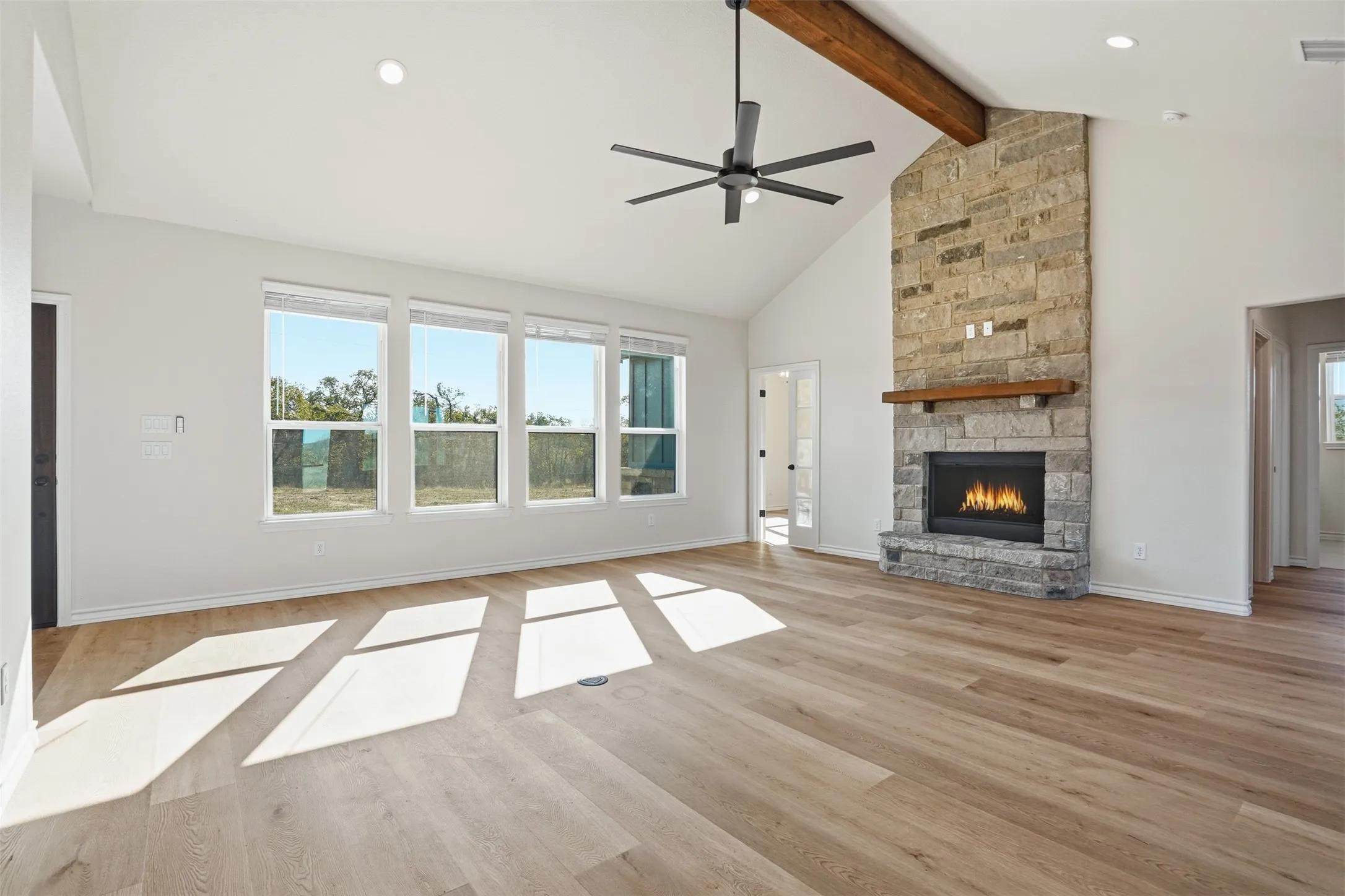 Unfurnished living room with high vaulted ceiling, a fireplace, light wood finished floors, a ceiling fan, and plenty of natural light