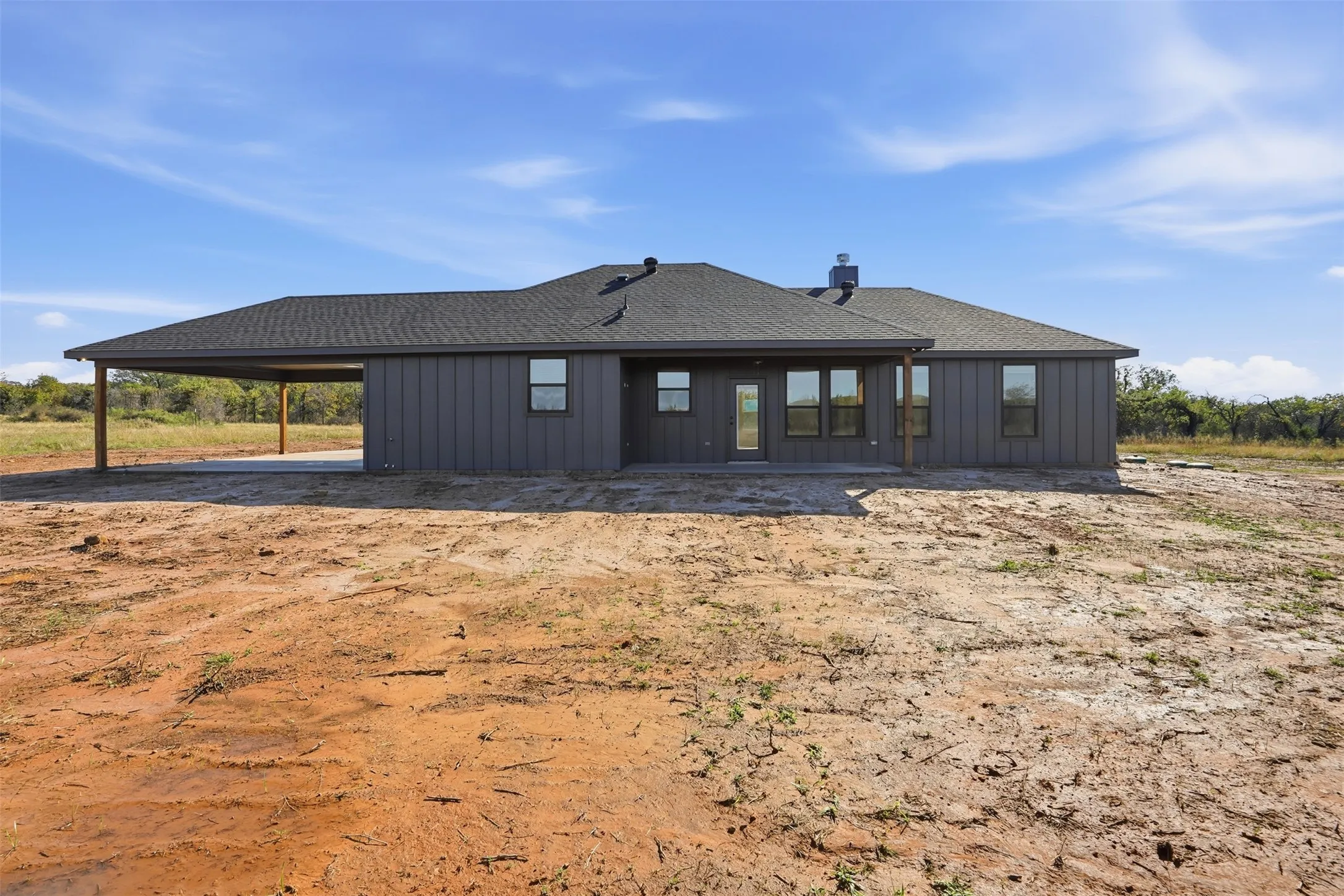 Rear view of property with roof with shingles, board and batten siding, a patio, and an attached carport