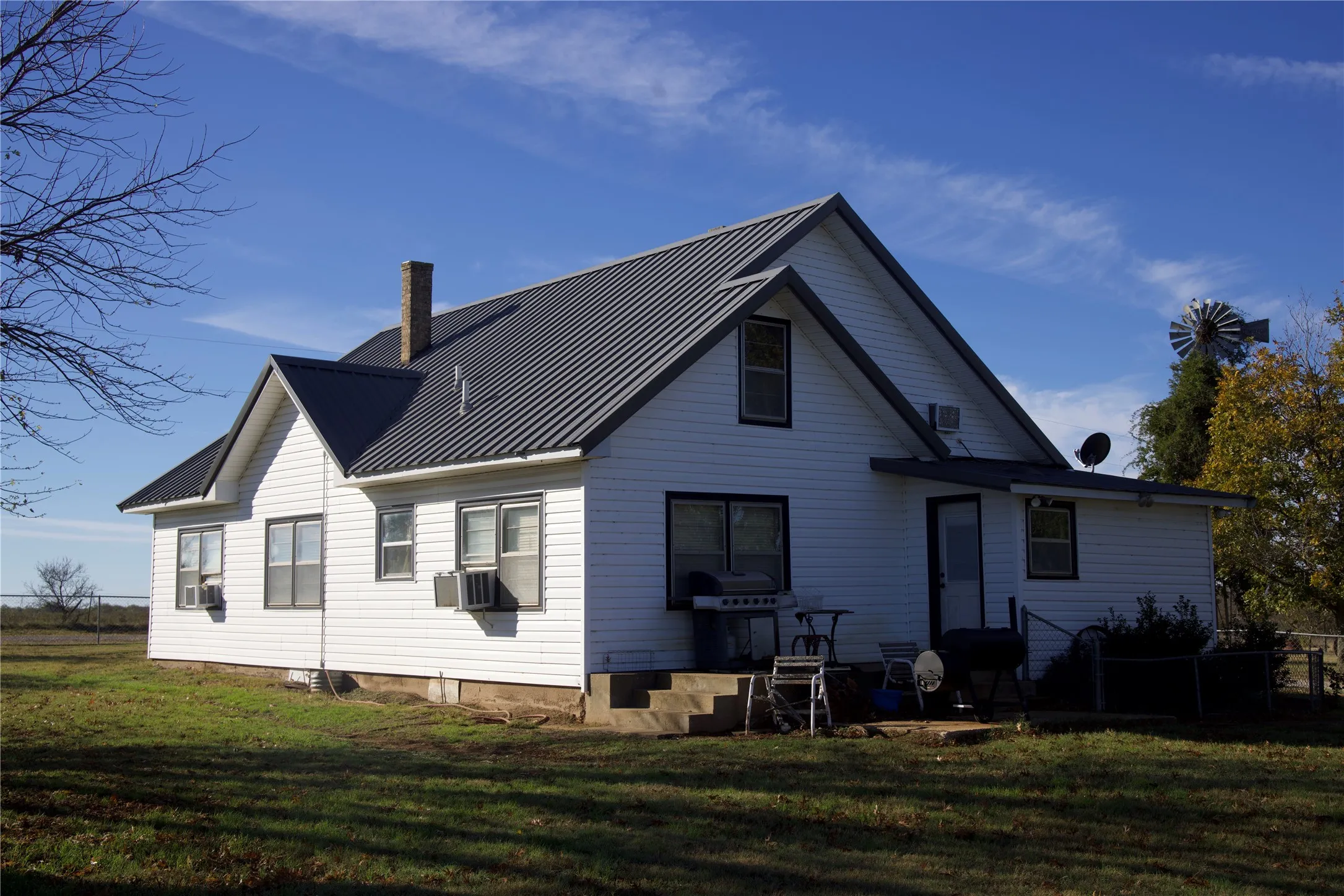 Rear view of property featuring a yard, a metal roof, a chimney, and cooling unit