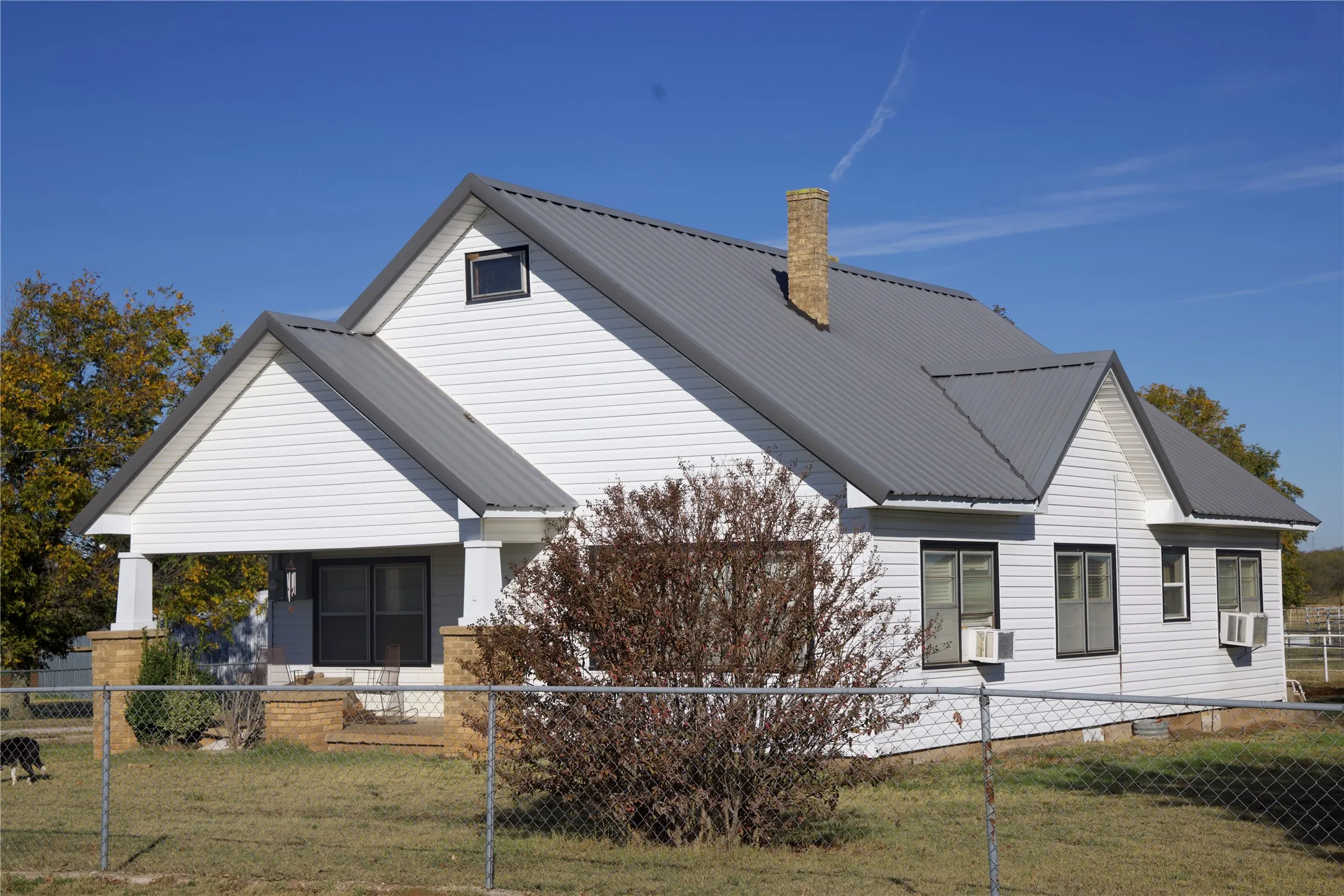 Back of property with a fenced front yard, a metal roof, a chimney, and cooling unit