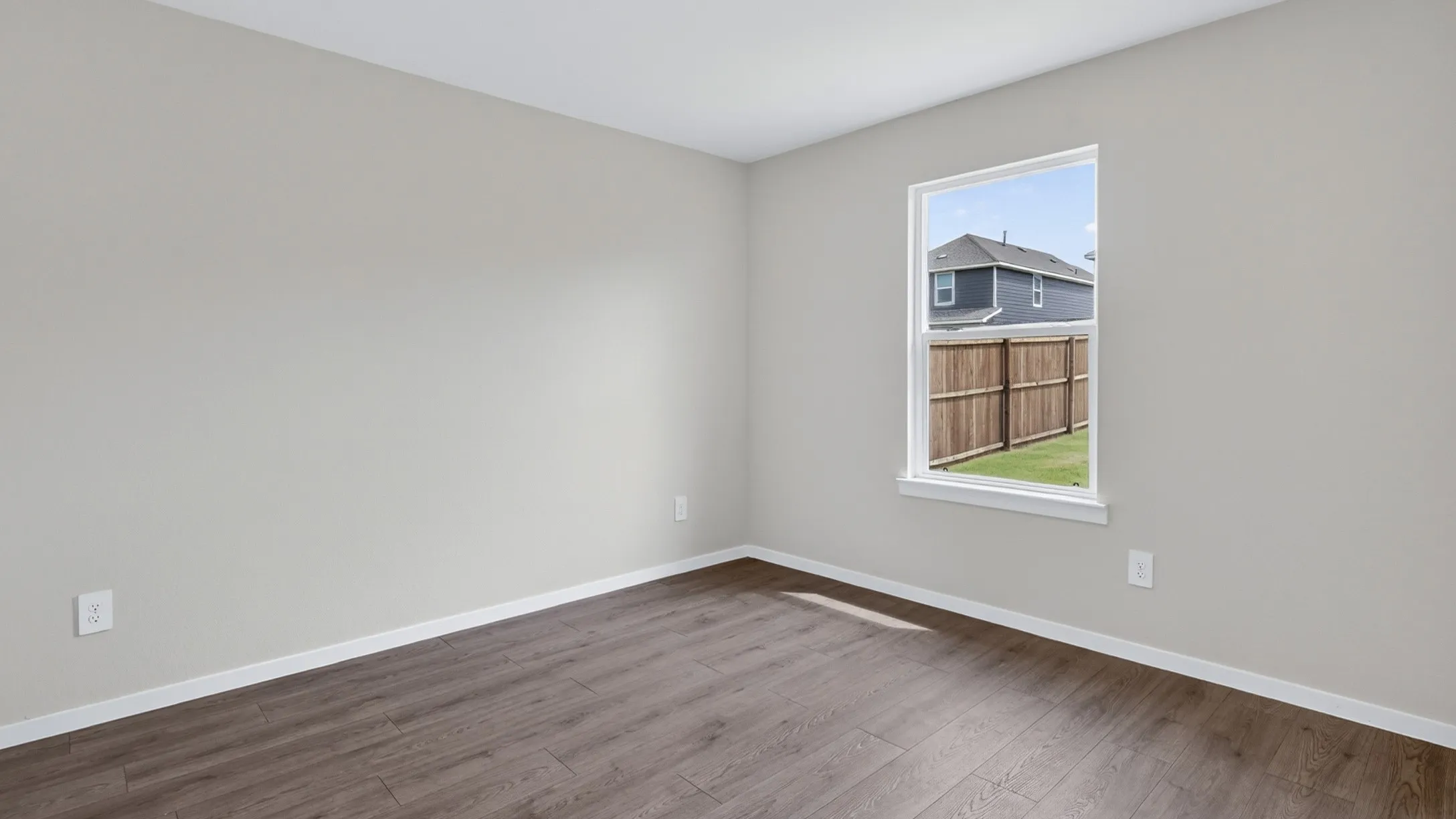 Spacious room featuring light gray walls, wood-finish flooring, and white baseboards