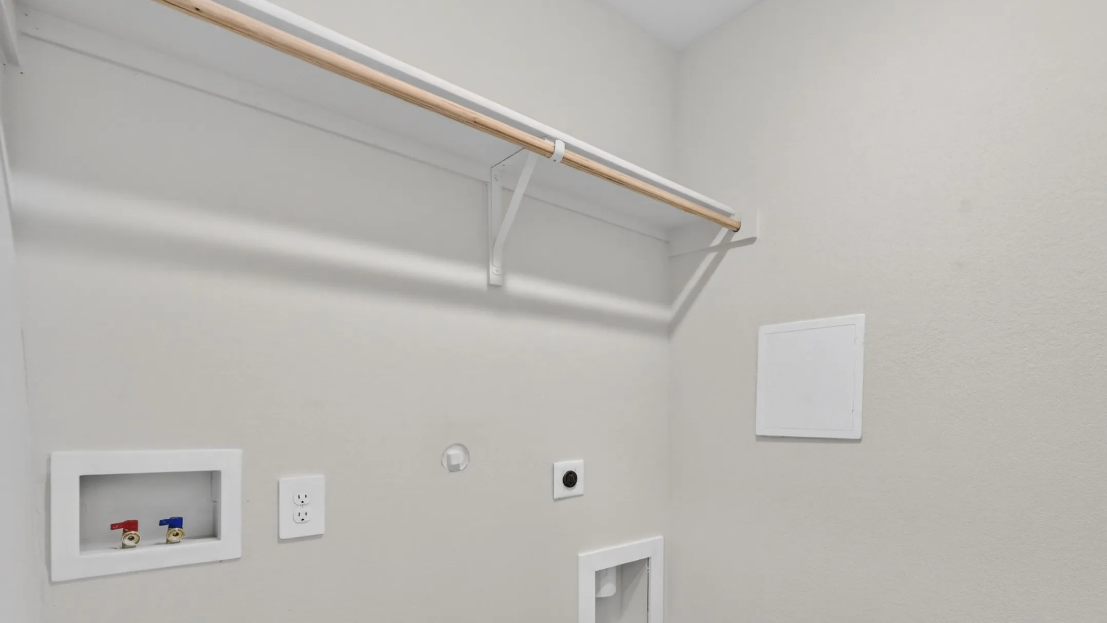 Dedicated laundry area featuring a built-in hanging rod, wall-mounted shelving, and utility hookups for appliances