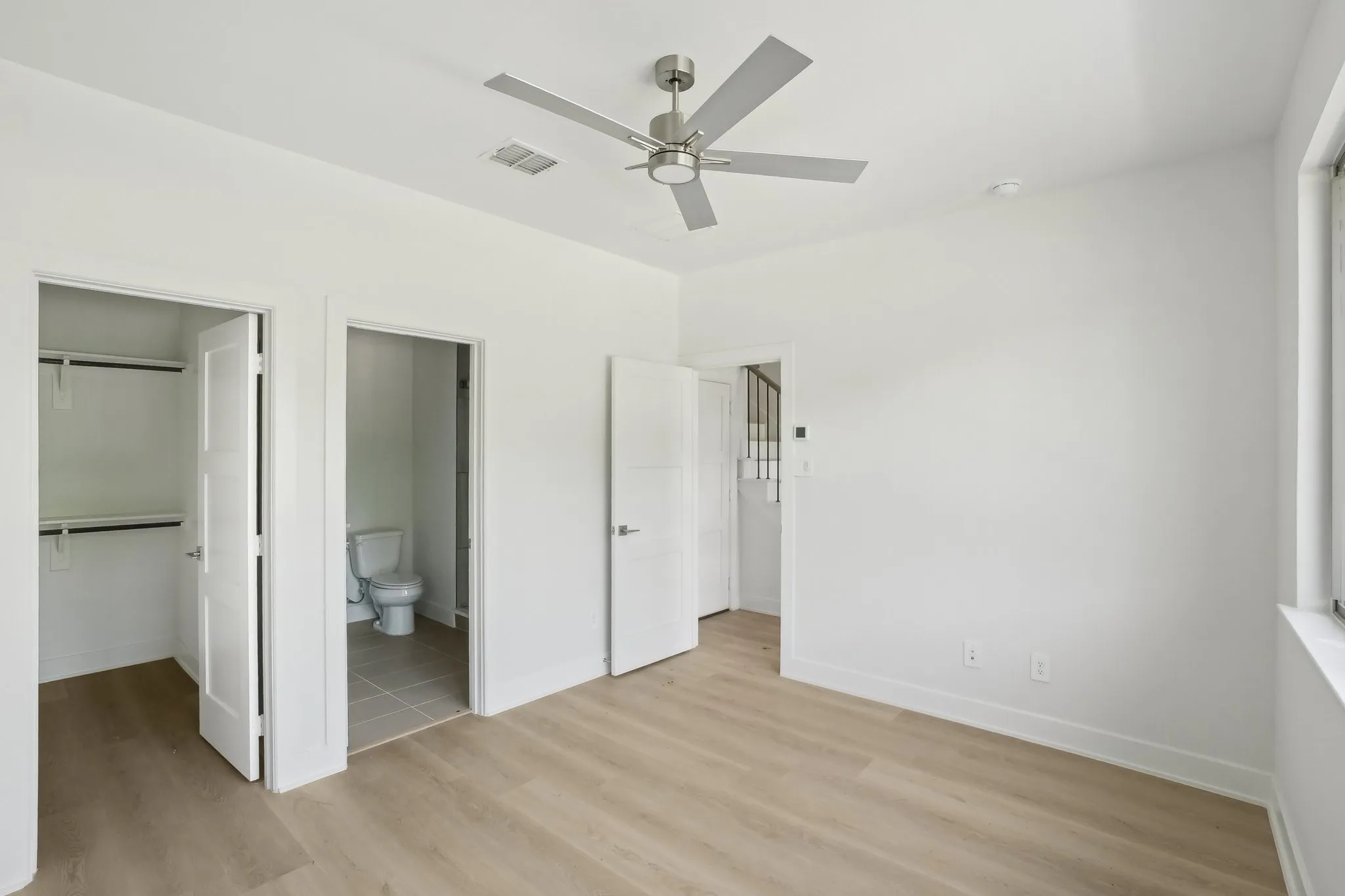 Unfurnished bedroom featuring light wood-style flooring, a walk in closet, a ceiling fan, and connected bathroom
