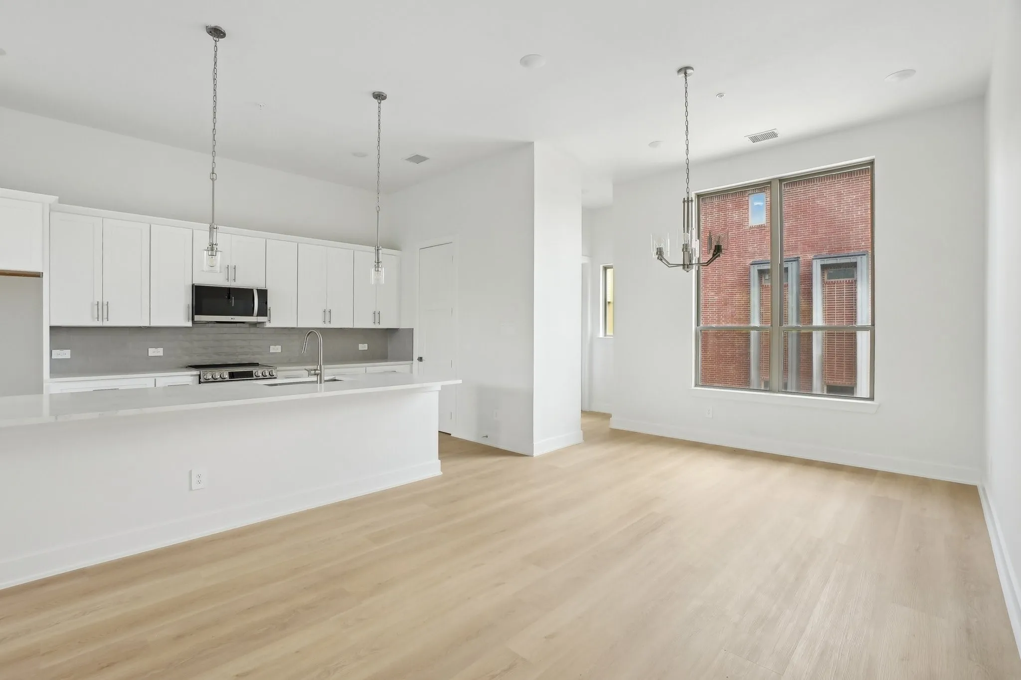 Kitchen with white cabinetry, decorative light fixtures, light wood-style floors, appliances with stainless steel finishes, and backsplash