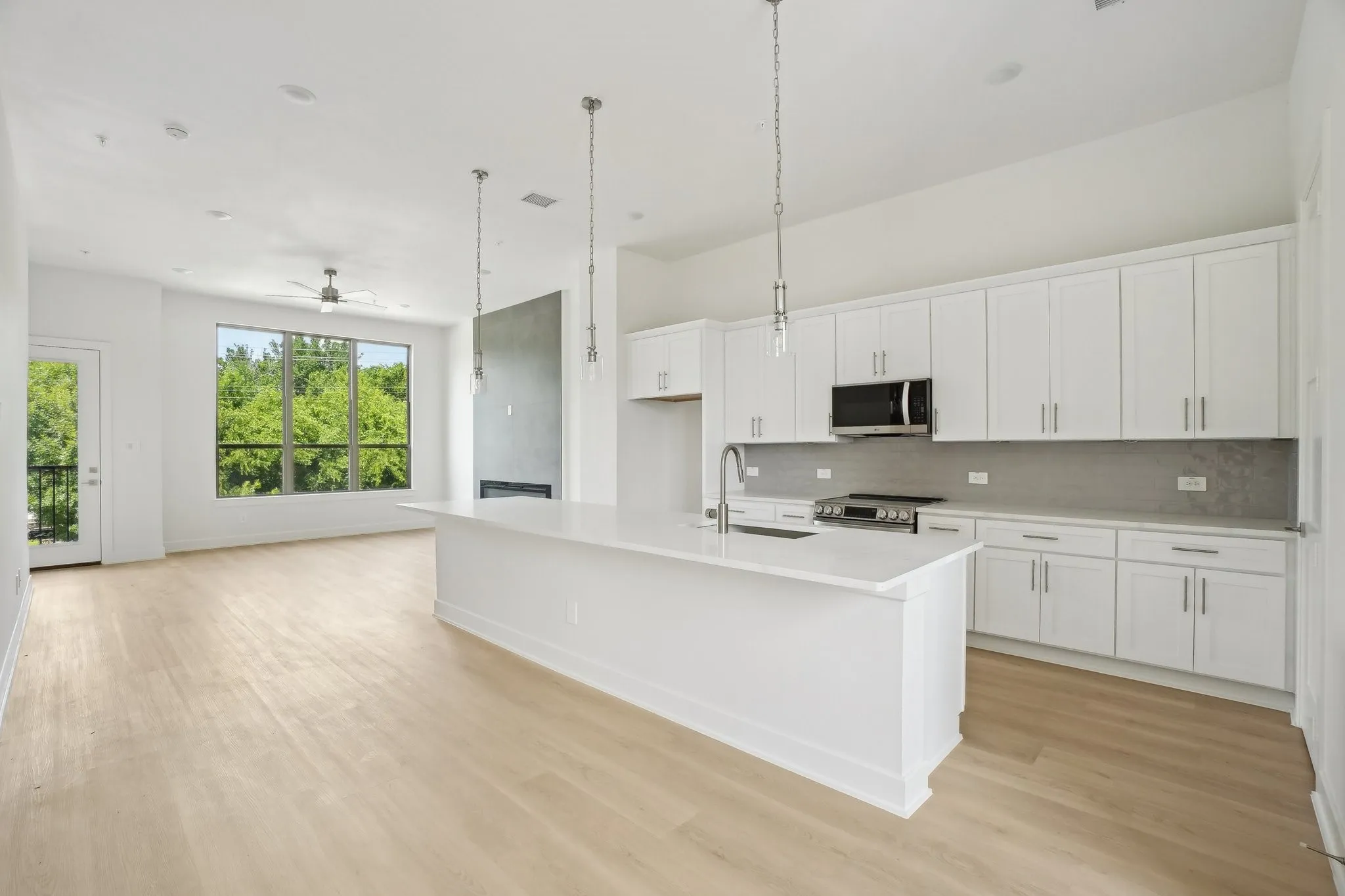 Kitchen featuring pendant lighting, white cabinets, a kitchen island with sink, backsplash, and stainless steel appliances