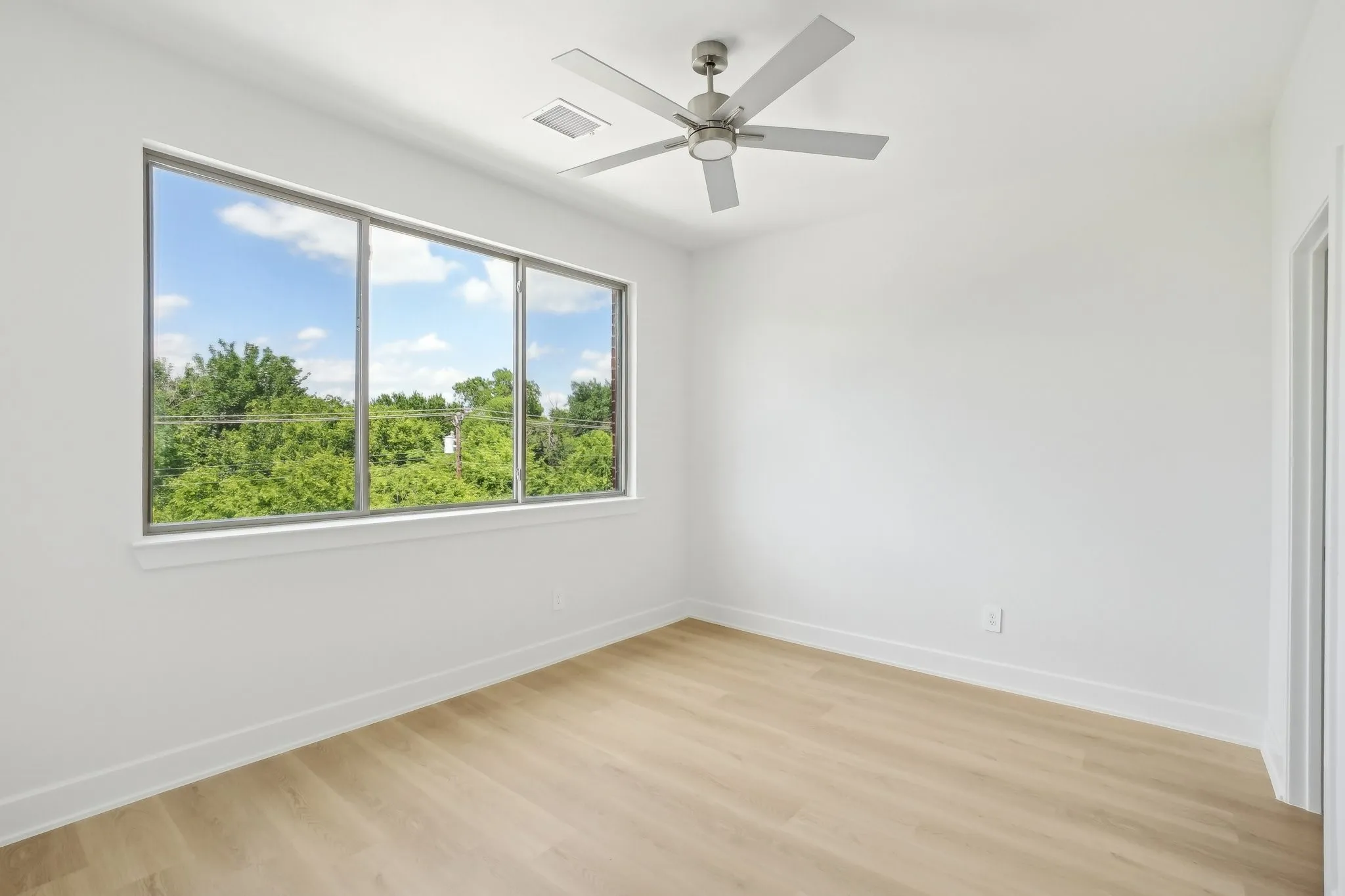 Unfurnished room featuring light wood-style flooring, a ceiling fan, and view of scattered trees