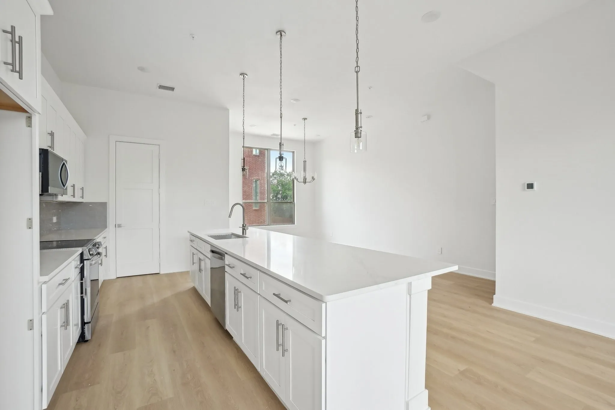 Kitchen with white cabinets, stainless steel appliances, light wood-style floors, an island with sink, and pendant lighting