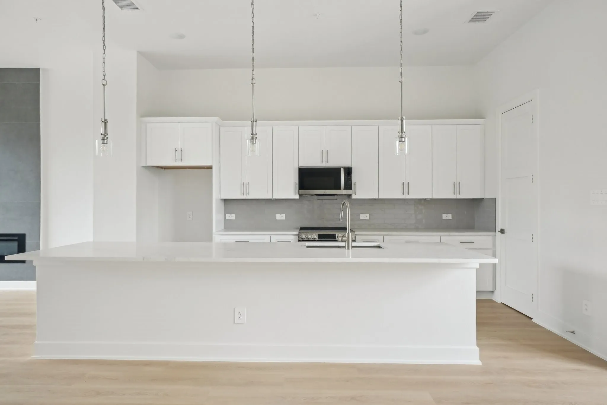 Kitchen with decorative light fixtures, white cabinetry, light wood-type flooring, a large island with sink, and stainless steel appliances