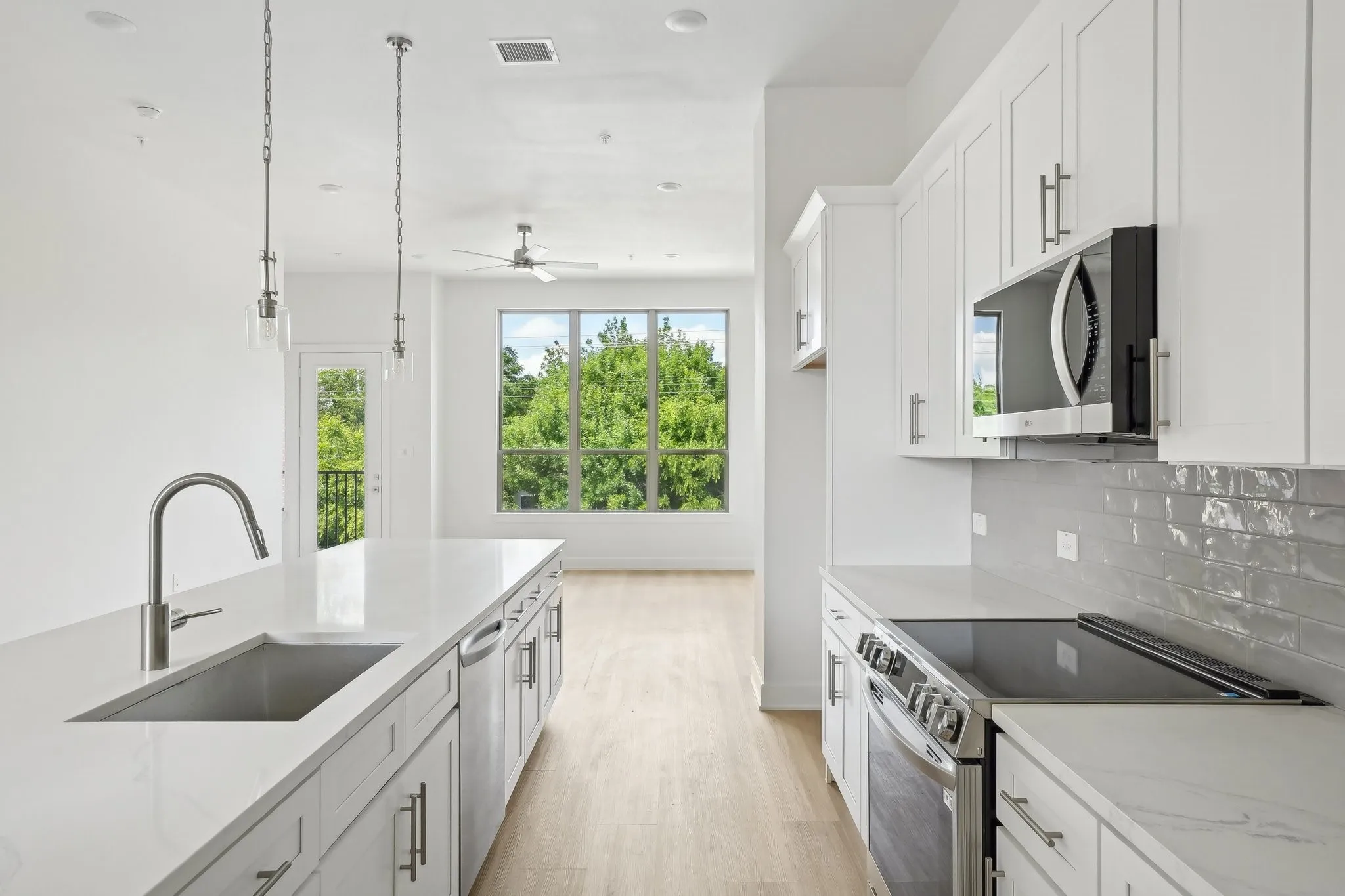 Kitchen with appliances with stainless steel finishes, hanging light fixtures, white cabinetry, light wood-style floors, and light stone counters