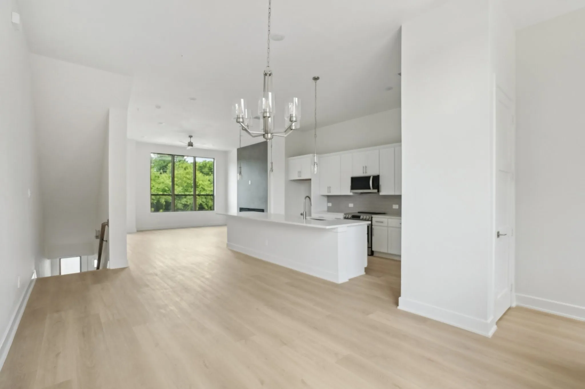 Kitchen with open floor plan, white cabinets, a center island with sink, pendant lighting, and a chandelier